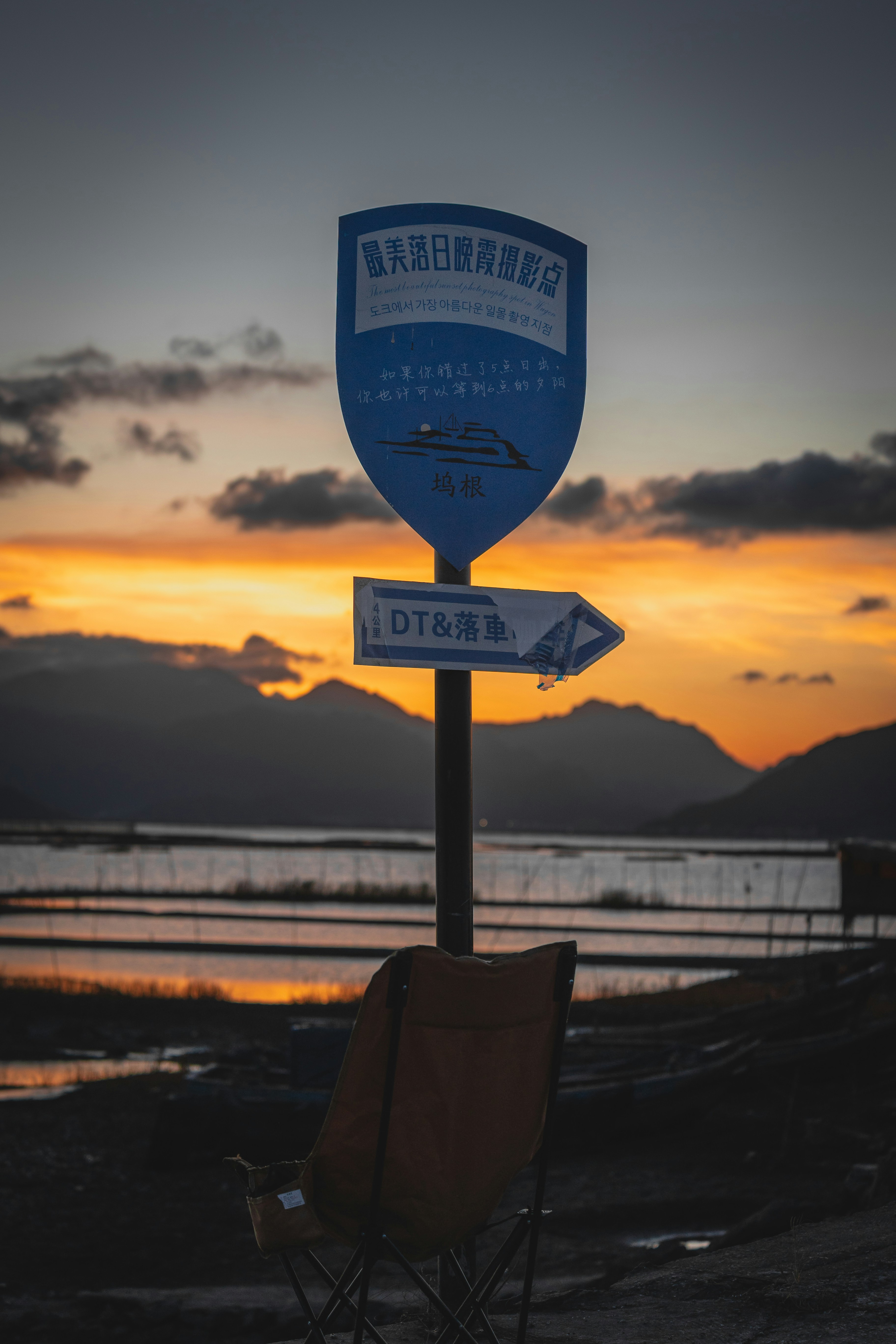 A placa de sinalização fica diante de um pôr do sol, com montanhas ao fundo.