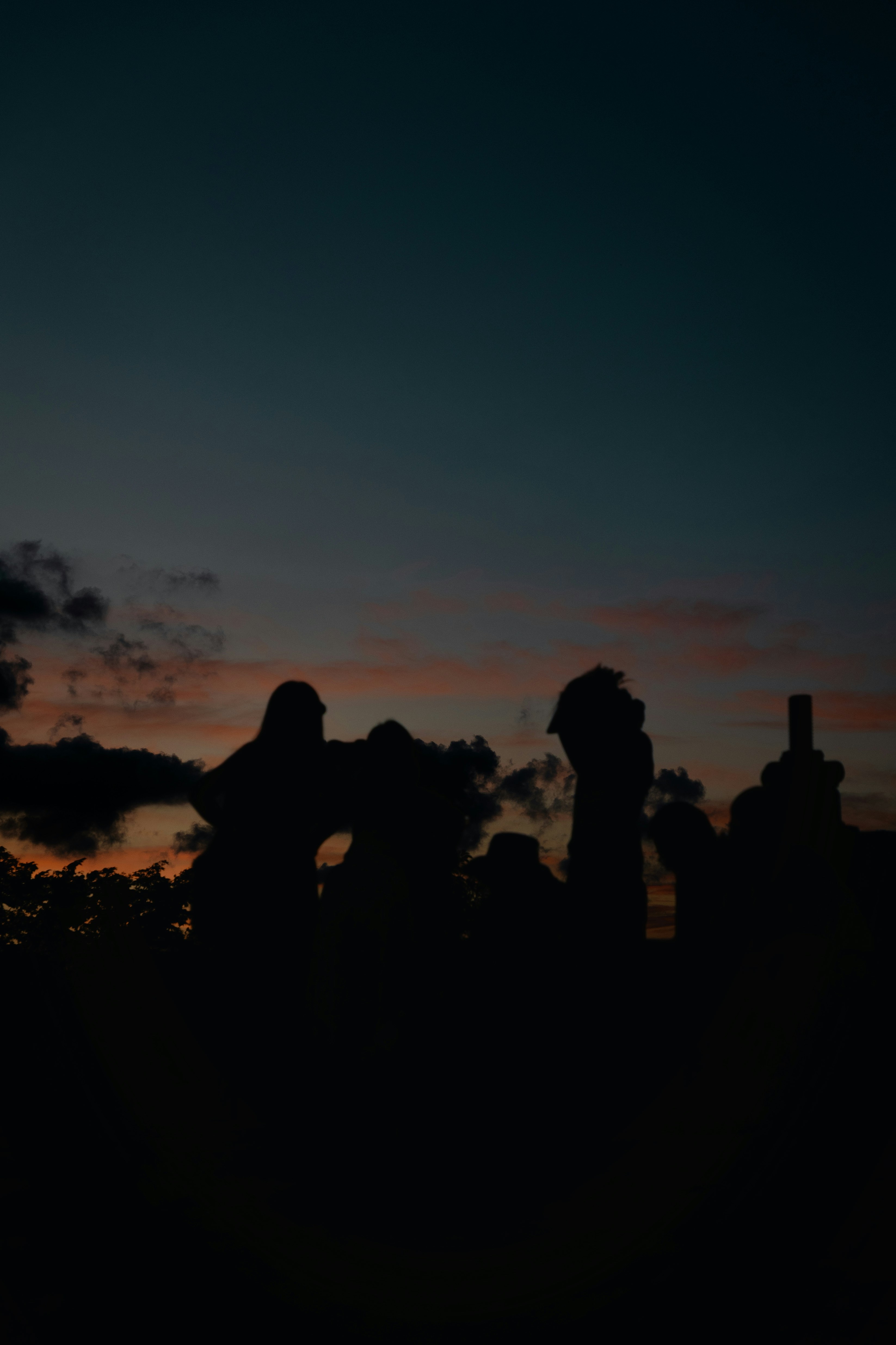 Pessoas em silhueta observam o pôr do sol.