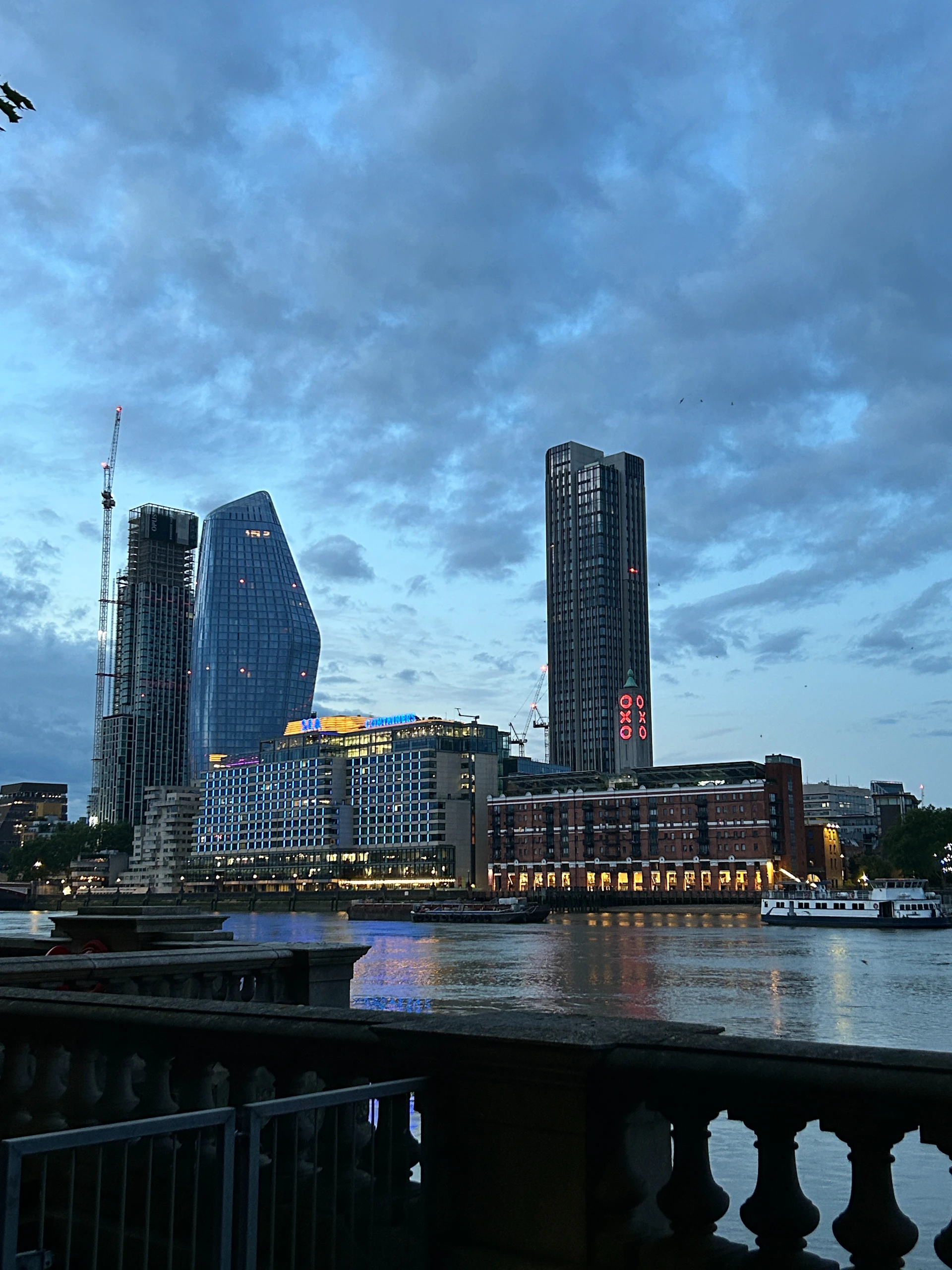 Skyscrapers line a river under a cloudy evening sky.