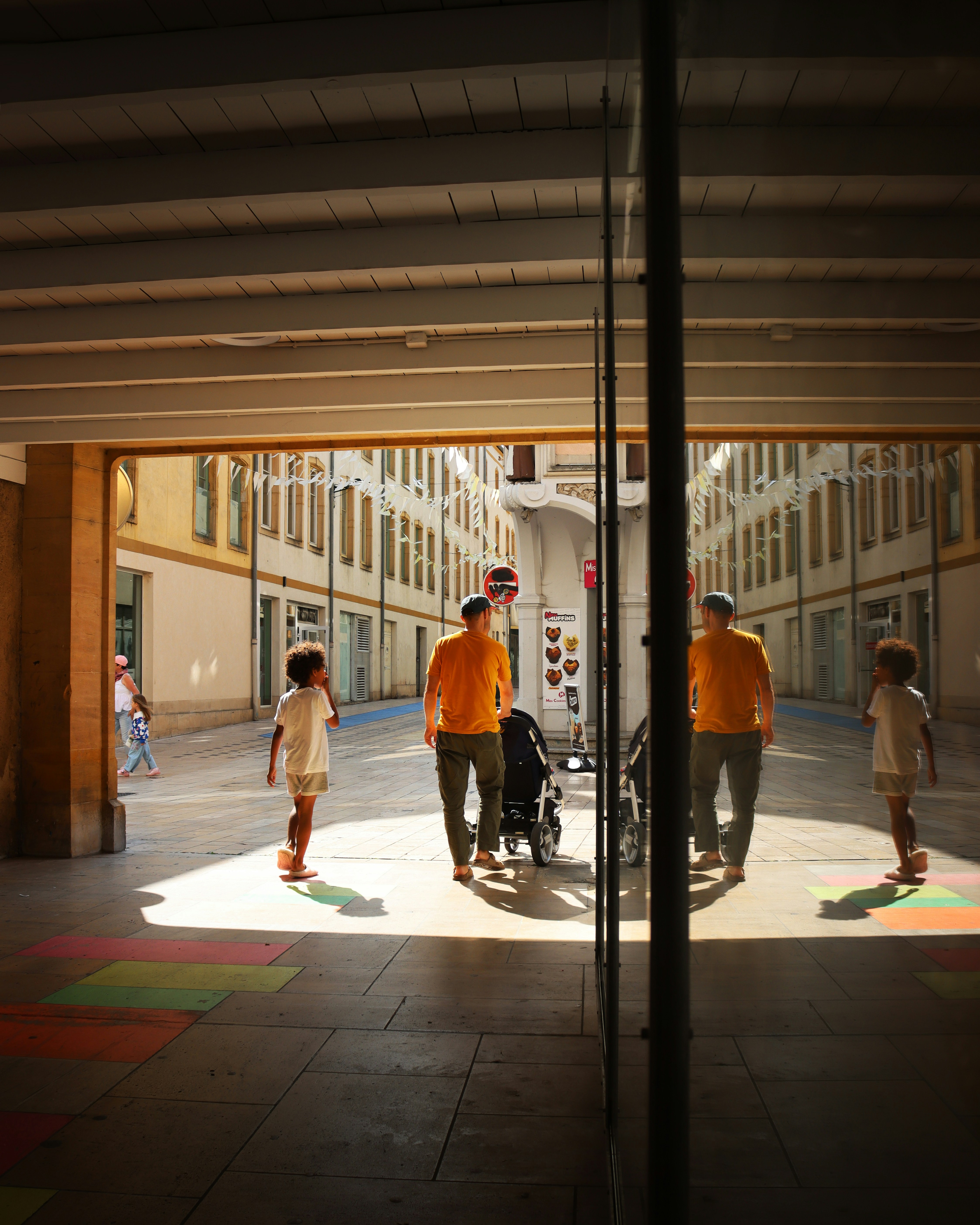Children walk beneath an arcade, reflected in glass.