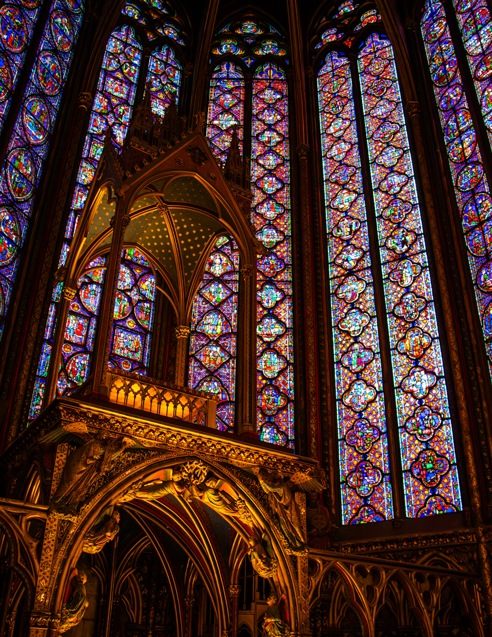 The image depicts a grand cathedral interior, with a large stained glass window dominating the scene. The window is composed of multiple panels, each exhibiting a different color and pattern, creating a vibrant display of hues that fill the space with light. The cathedral's architectural style is evident in its pointed arches and intricate details, which are accentuated by the golden accents on the ceiling and walls.

In addition to the stained glass window, there is also a small tower situated within the cathedral. This tower features a balcony adorned with gold accents, adding an element of luxury and grandeur to the space. The overall atmosphere of the cathedral is one of awe-inspiring beauty and tranquility, inviting visitors to explore its many wonders.