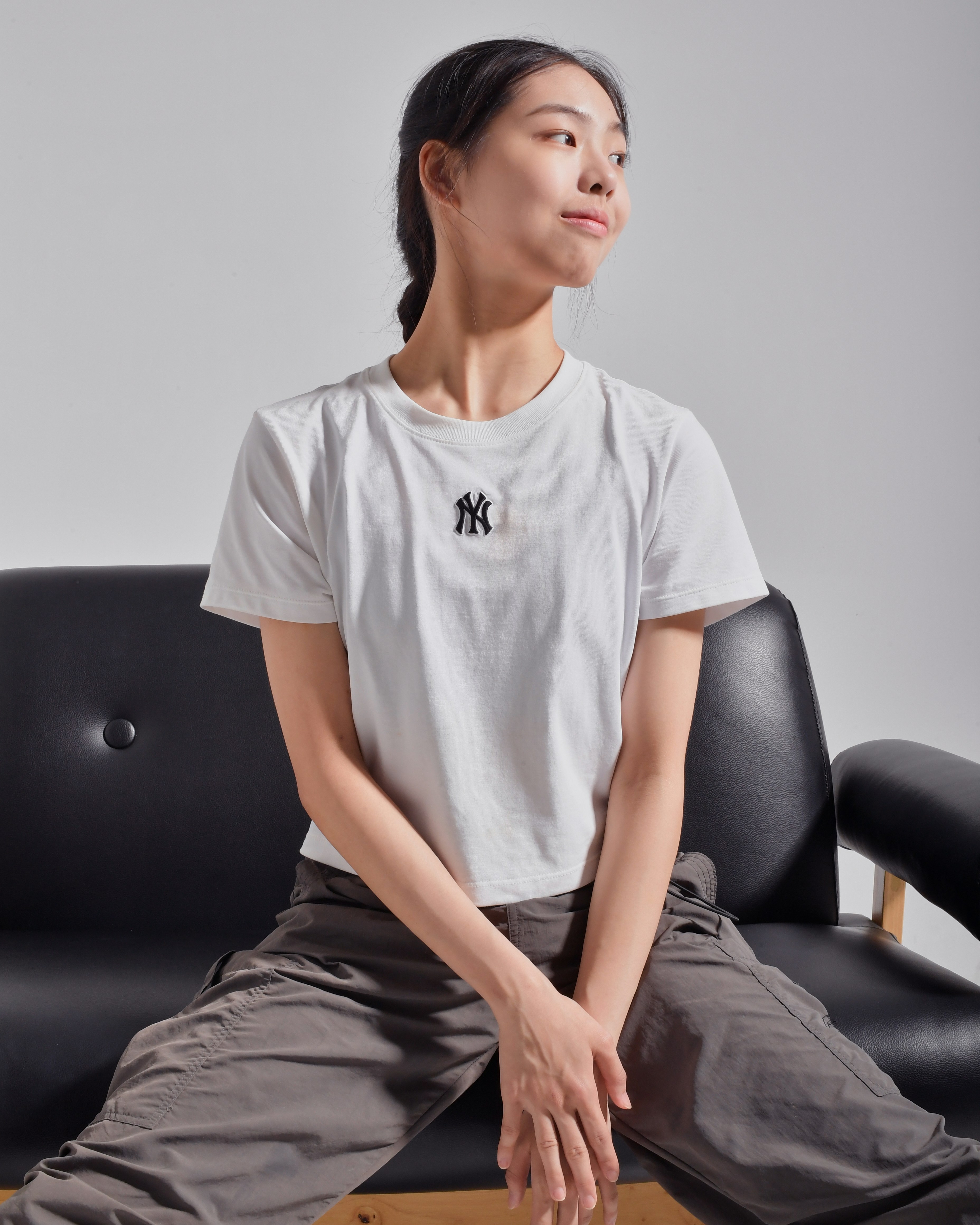Woman in white tee poses on a black couch.