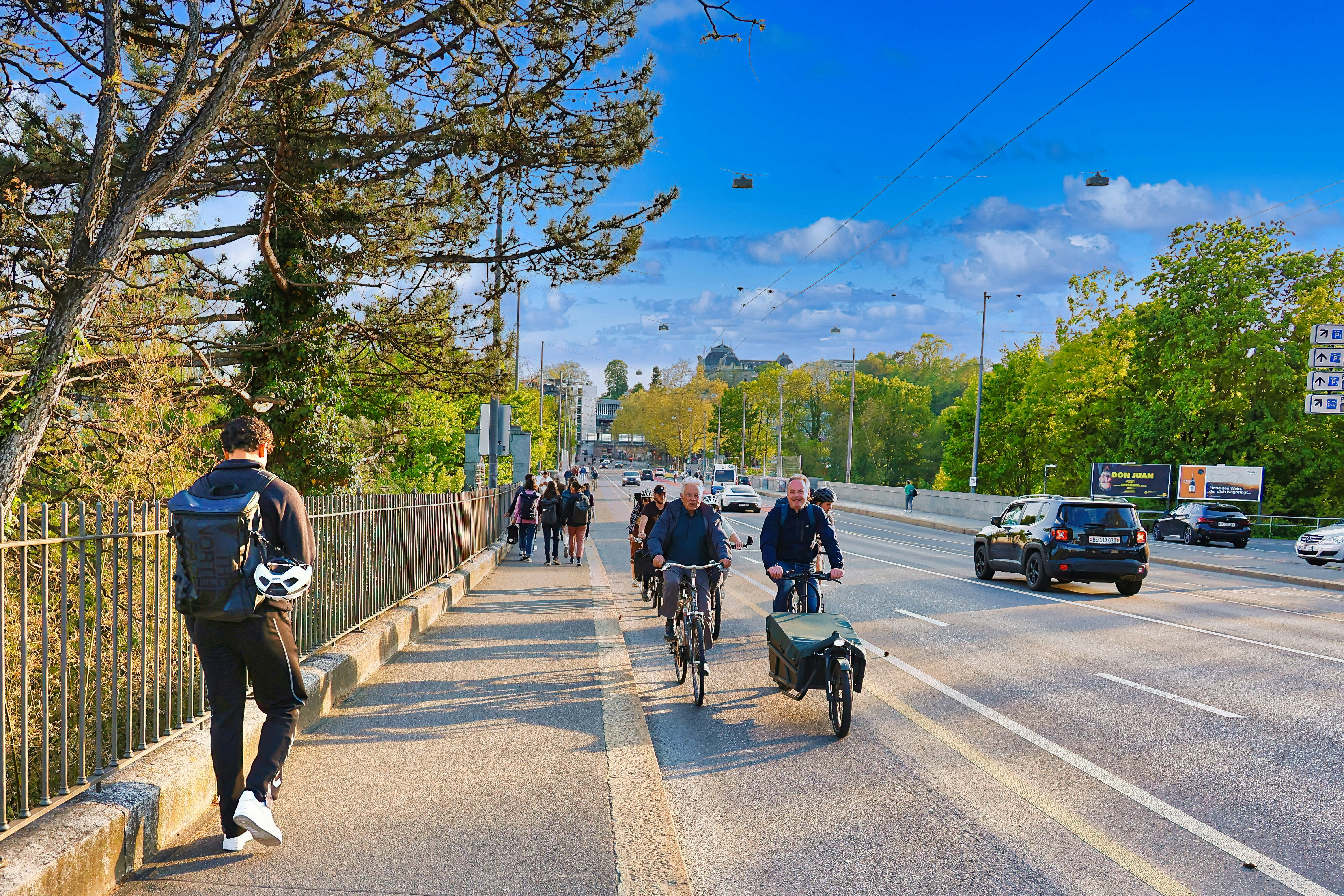 People walk and cycle along a sunny urban street.