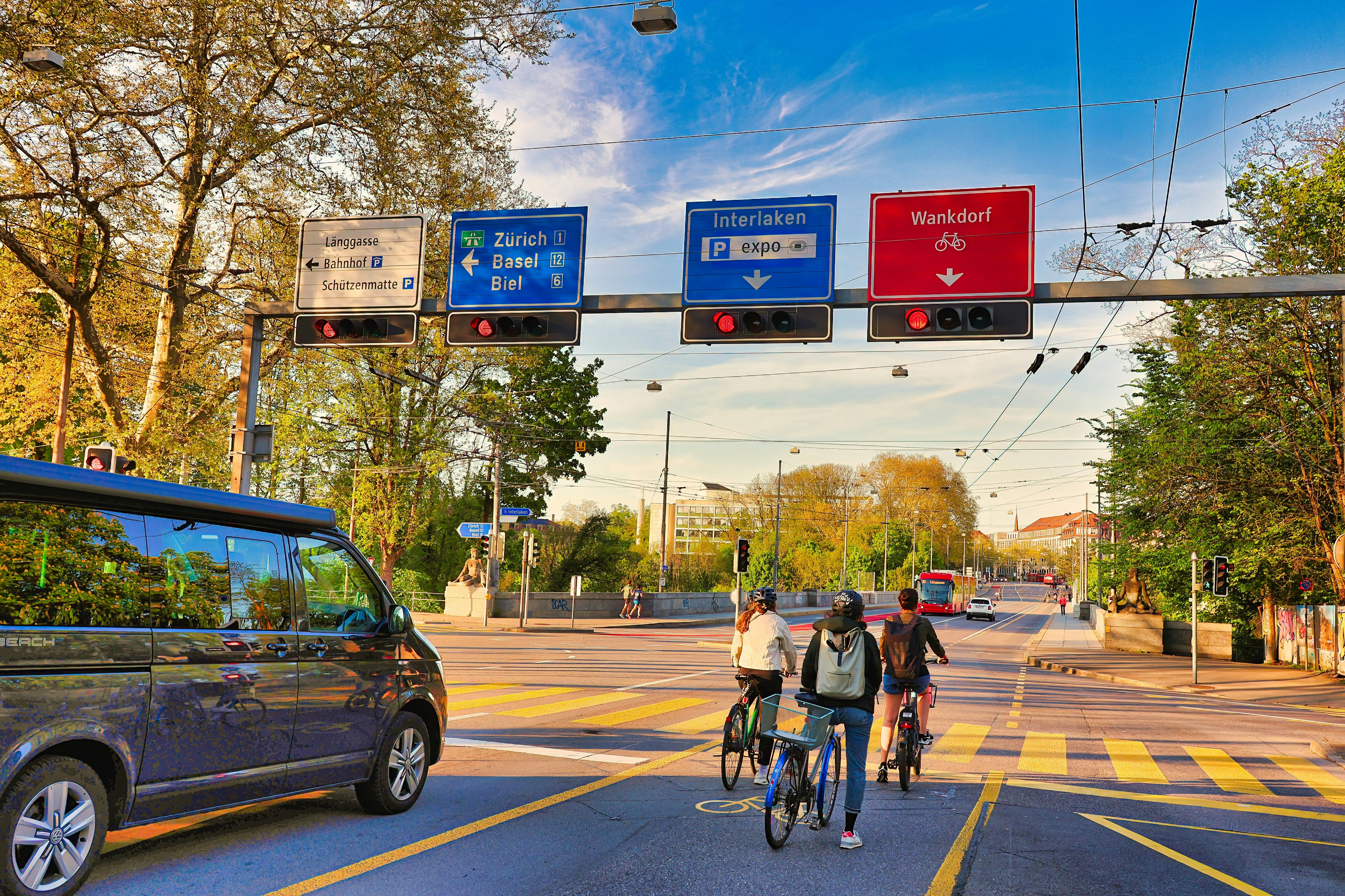 Cyclists ride by street signs on a sunny day.