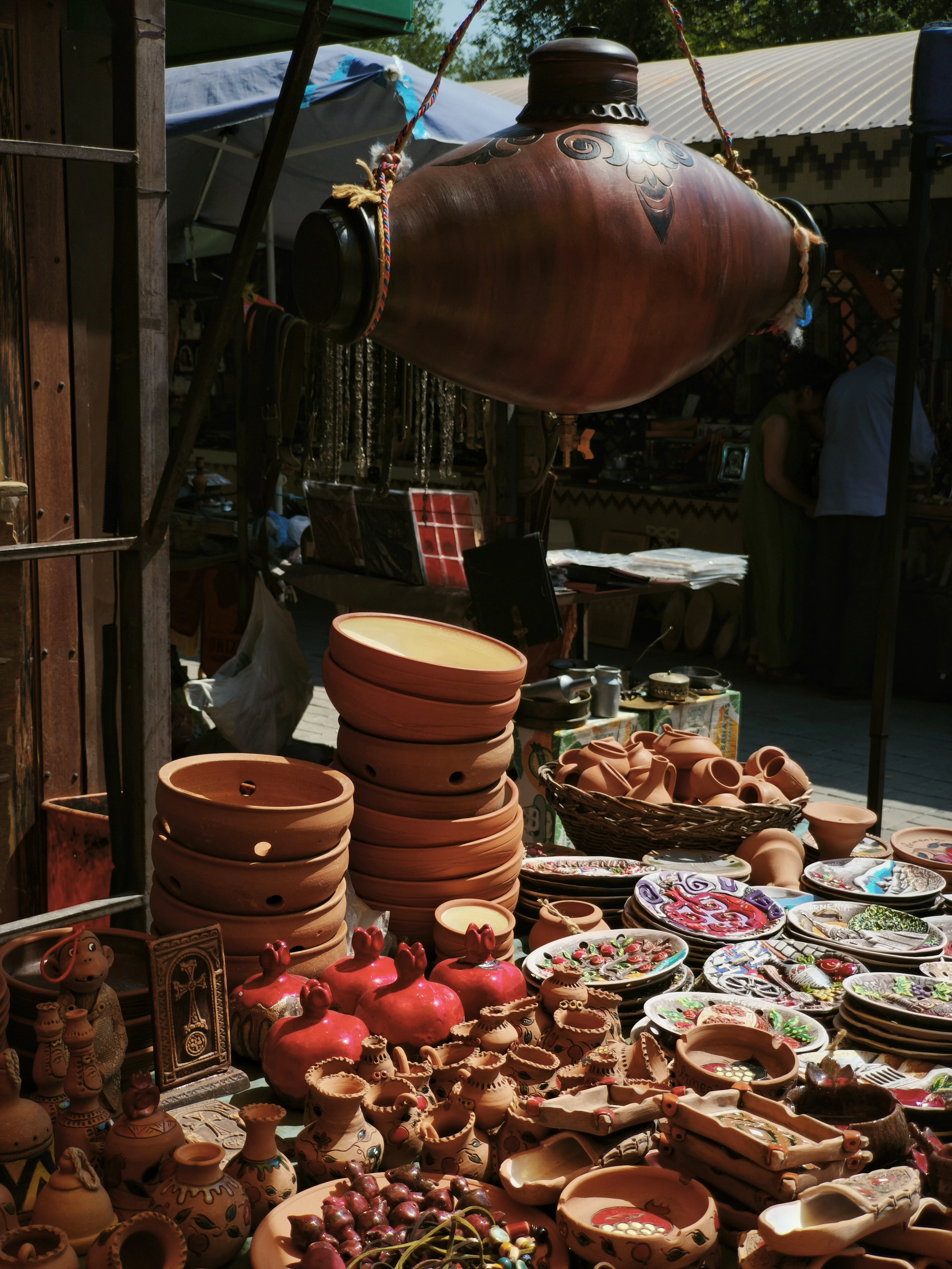 A stall at the Vernissage open-air market in Yerevan stacked with Armenian terracotta pots, painted ceramic plates and a large decorated jug hanging overhead.