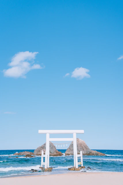 White torii gate stands in the ocean.