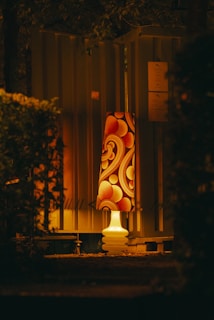 Градинска лампа с орнаменти, светеща в тъмната нощ.