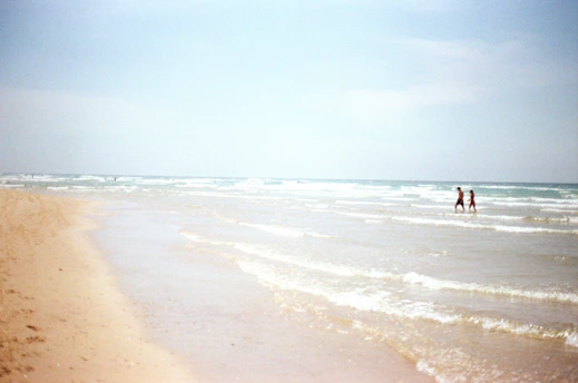 Two people walk along a beach.
