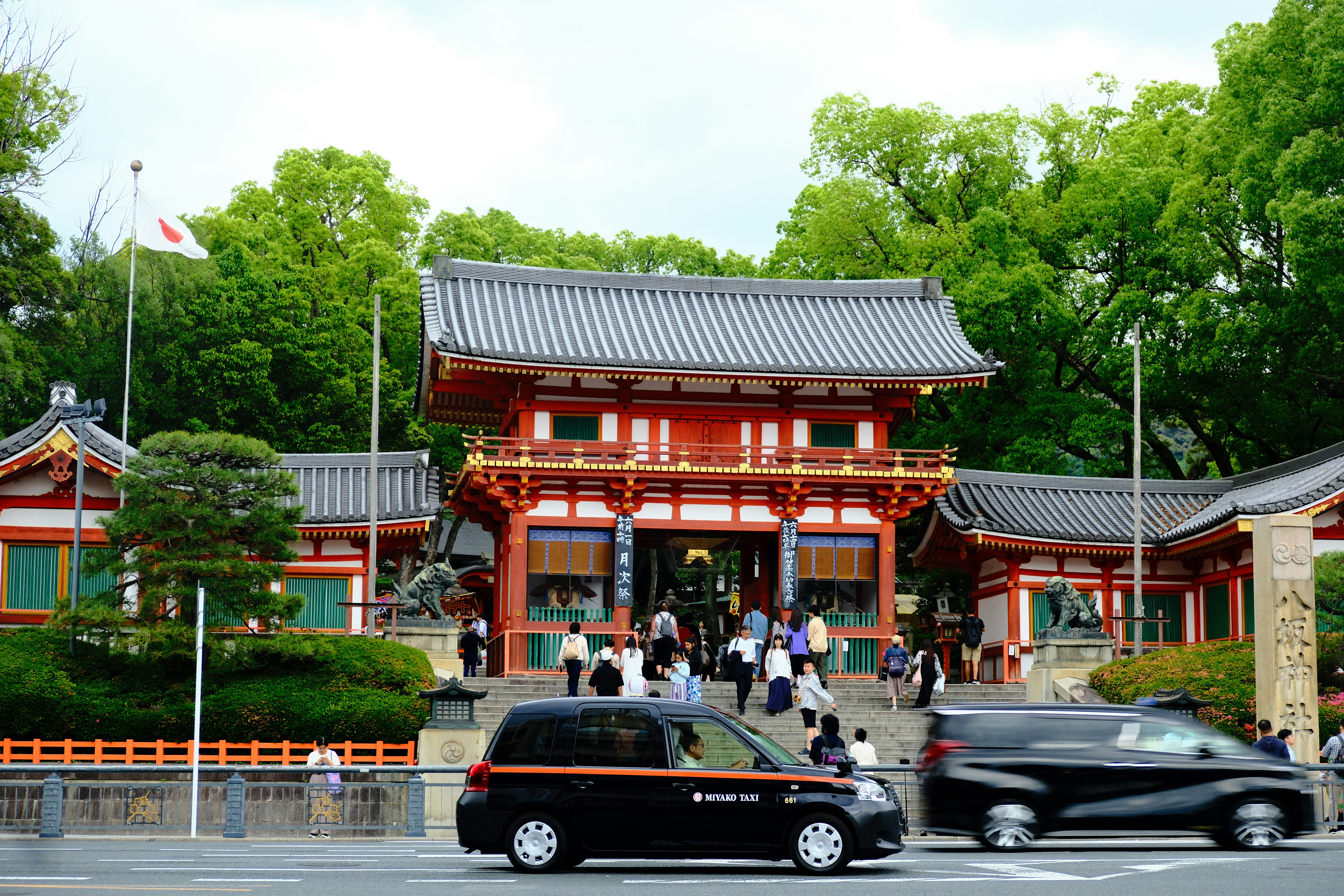A japanese temple is seen with cars passing by.