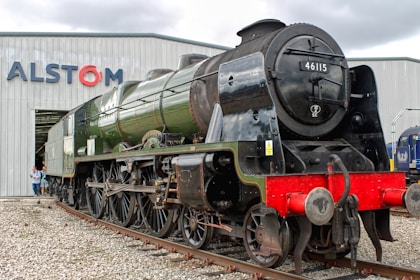 A green steam train stands in front of a building.