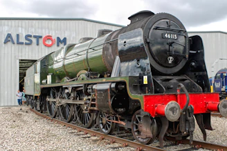 A green steam train stands in front of a building.