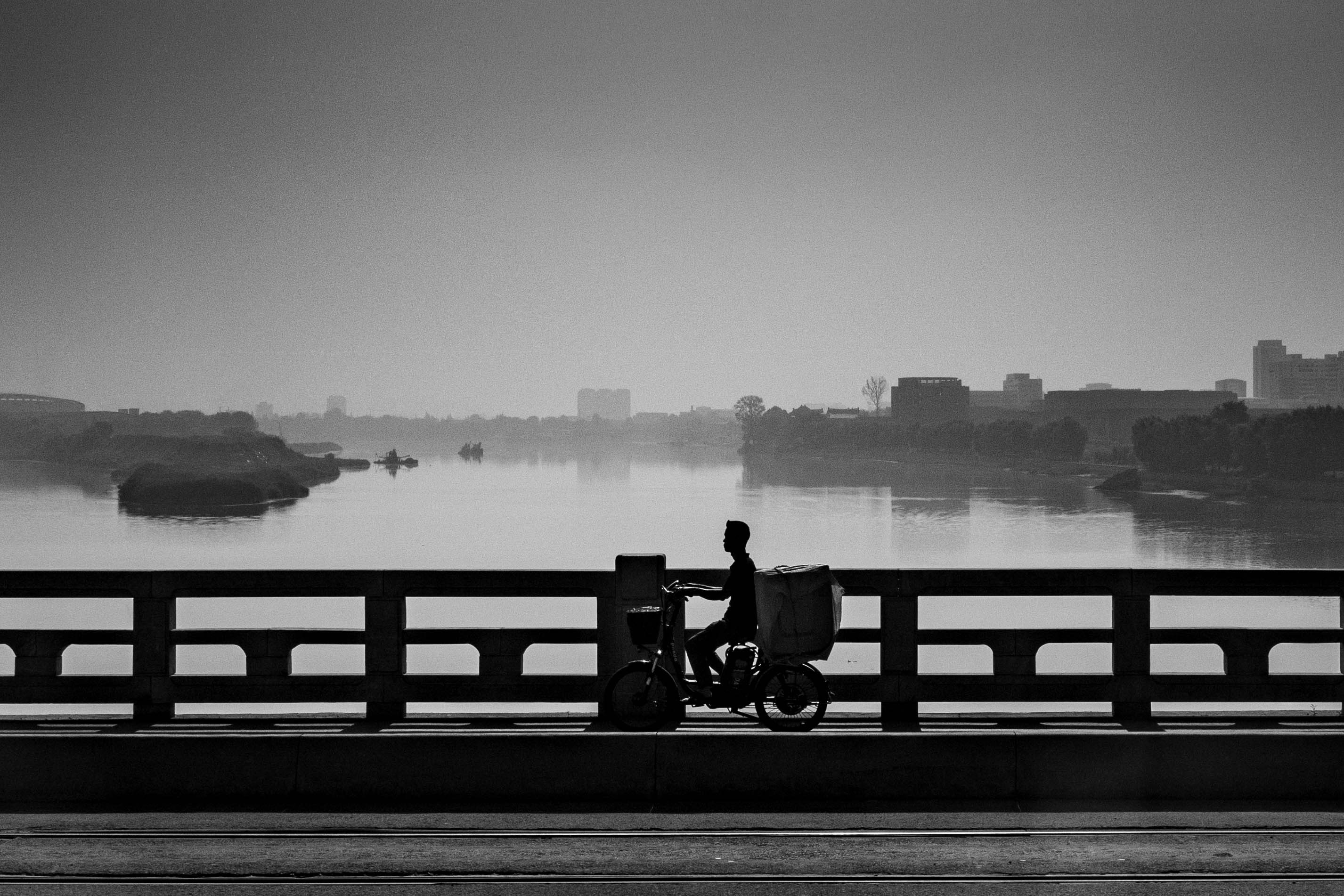 Cyclist silhouetted on bridge, delivering.