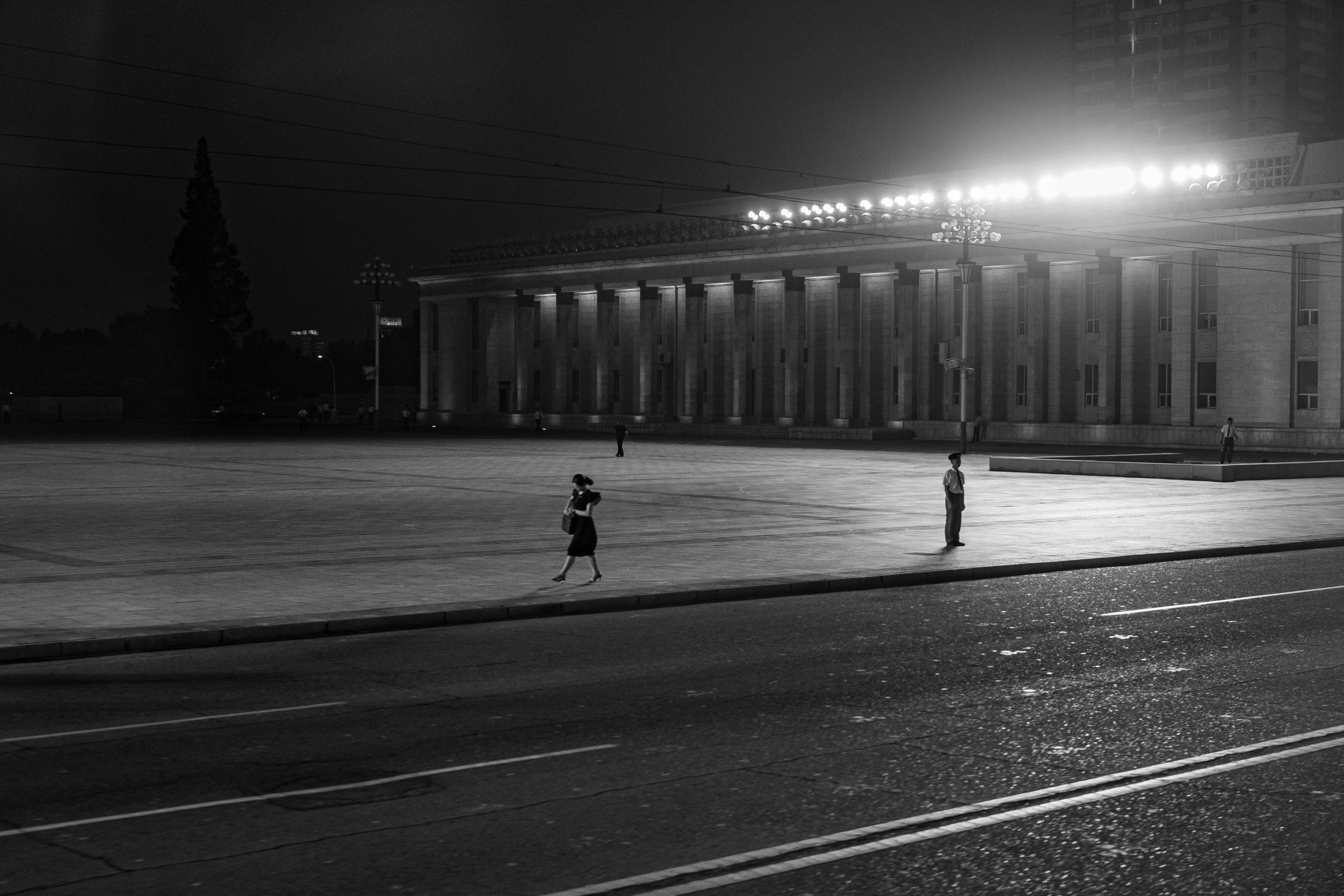 Two figures stand by a large, illuminated building.