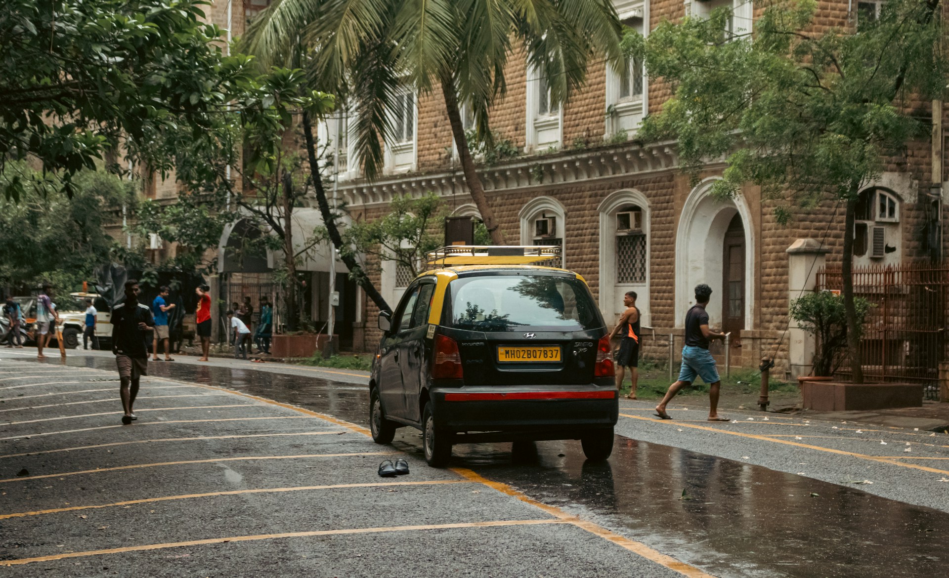 A yellow taxi and people on a wet street.