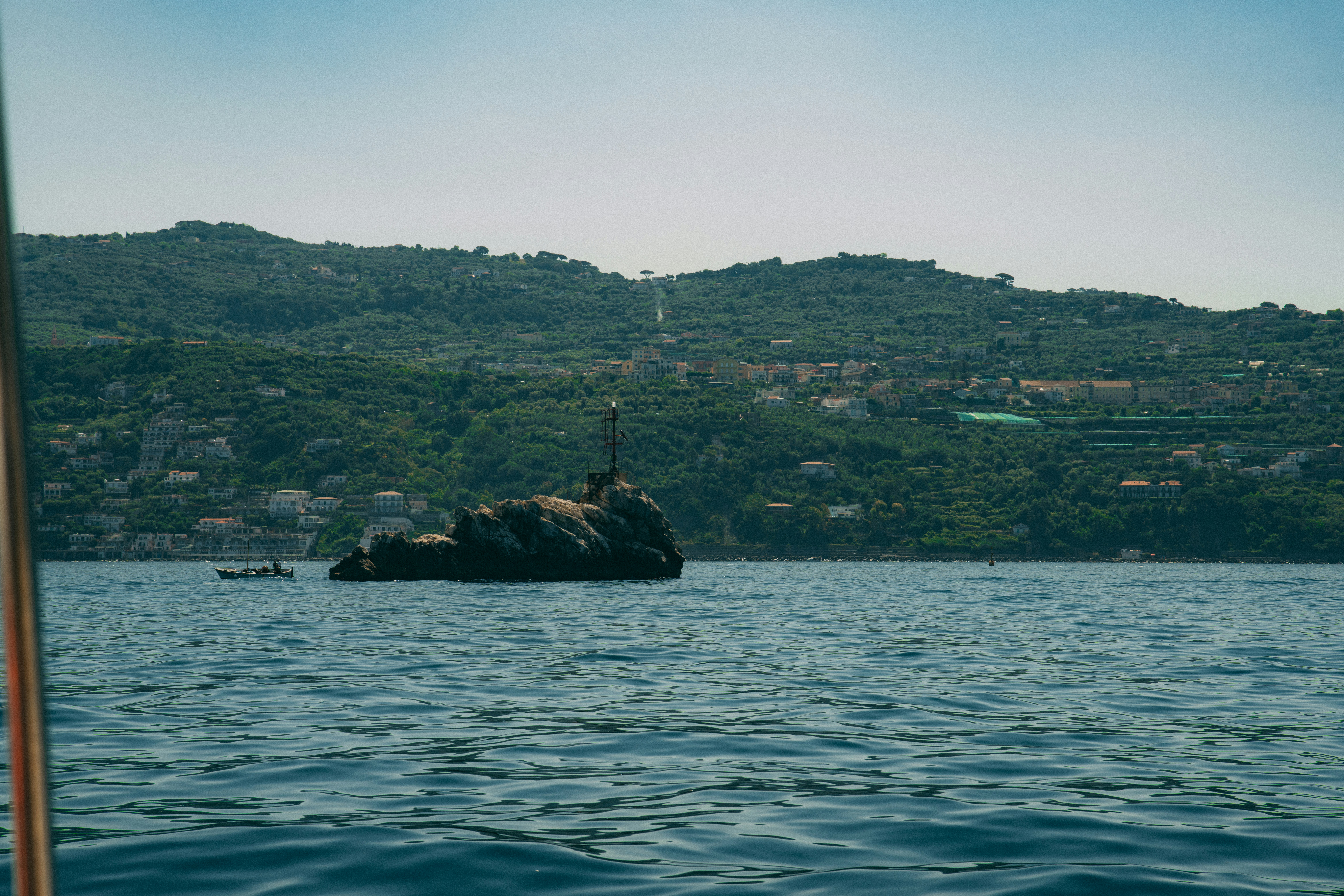 Rocky island sits in the ocean with mountainous background.