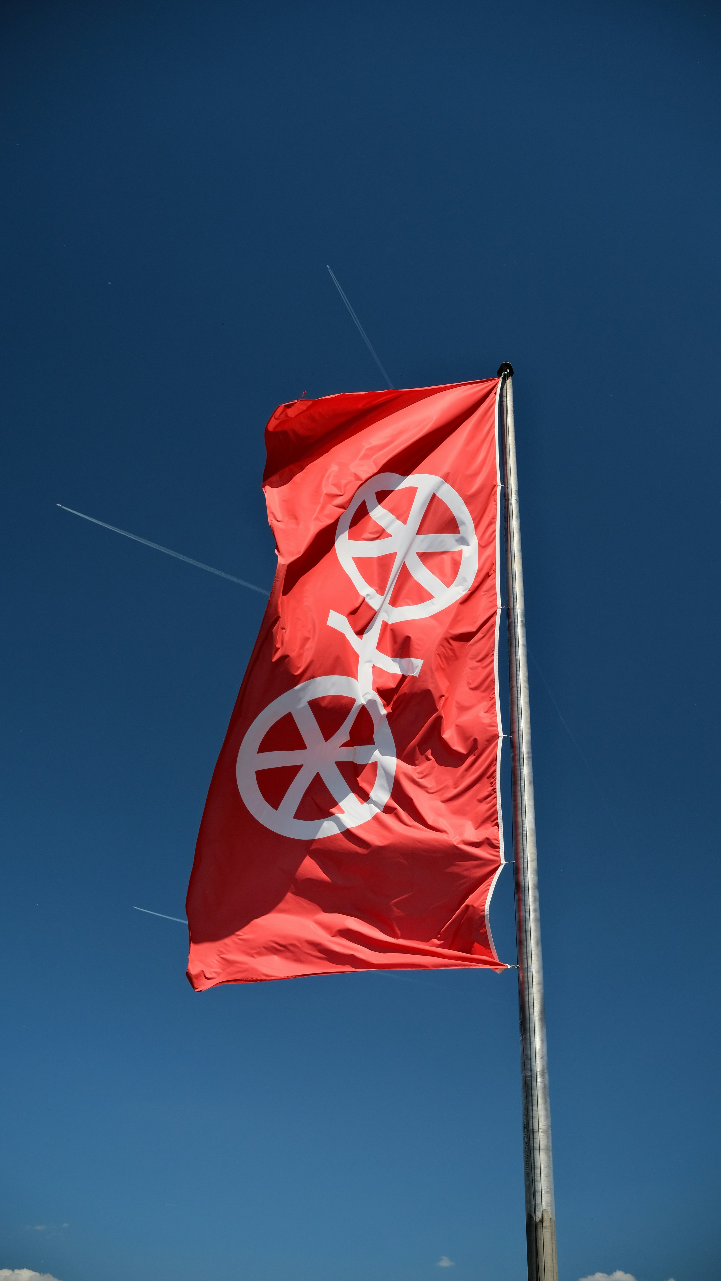 A red flag with a white symbol flies in the sky.