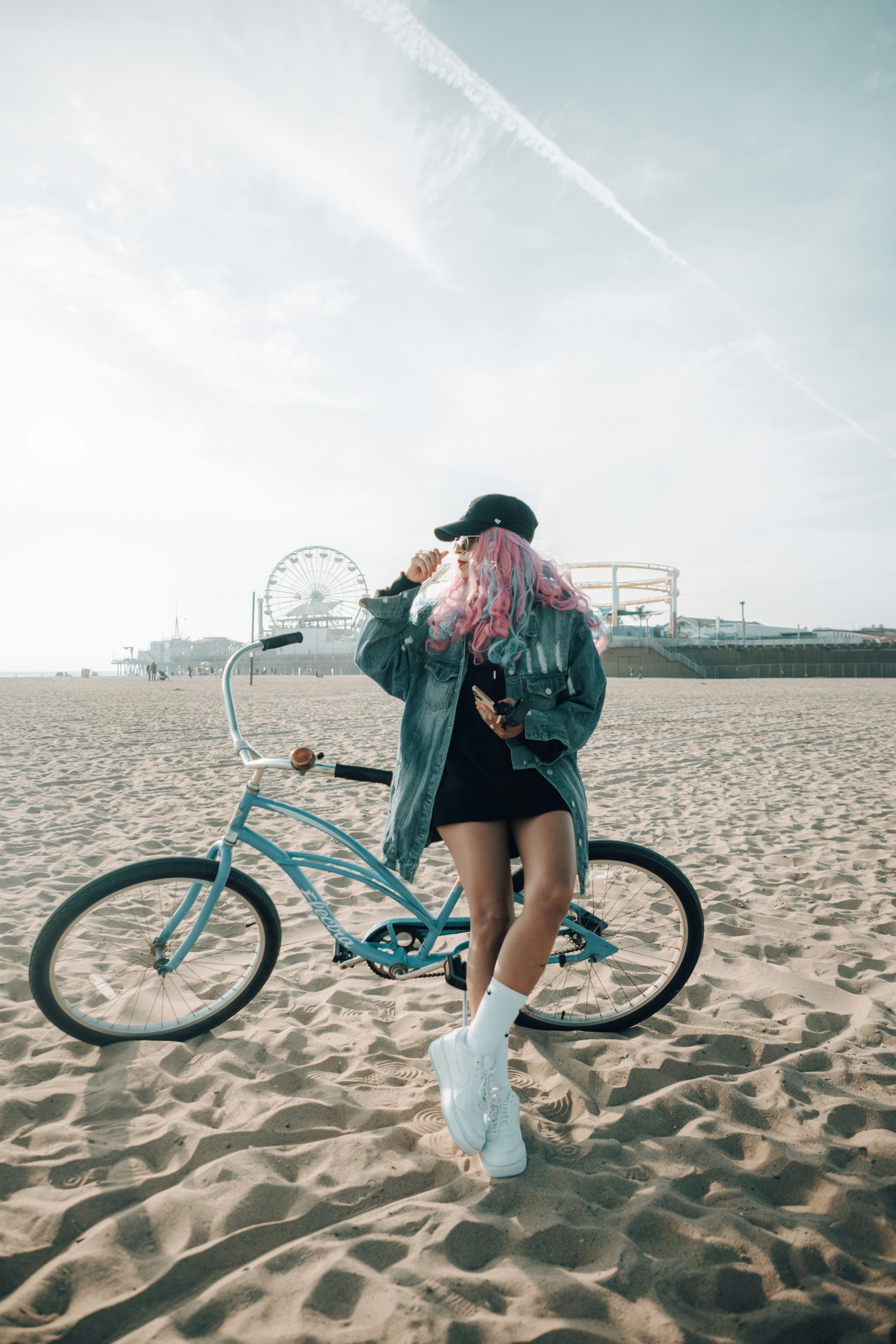 Woman with pink hair posing near a bicycle on the beach