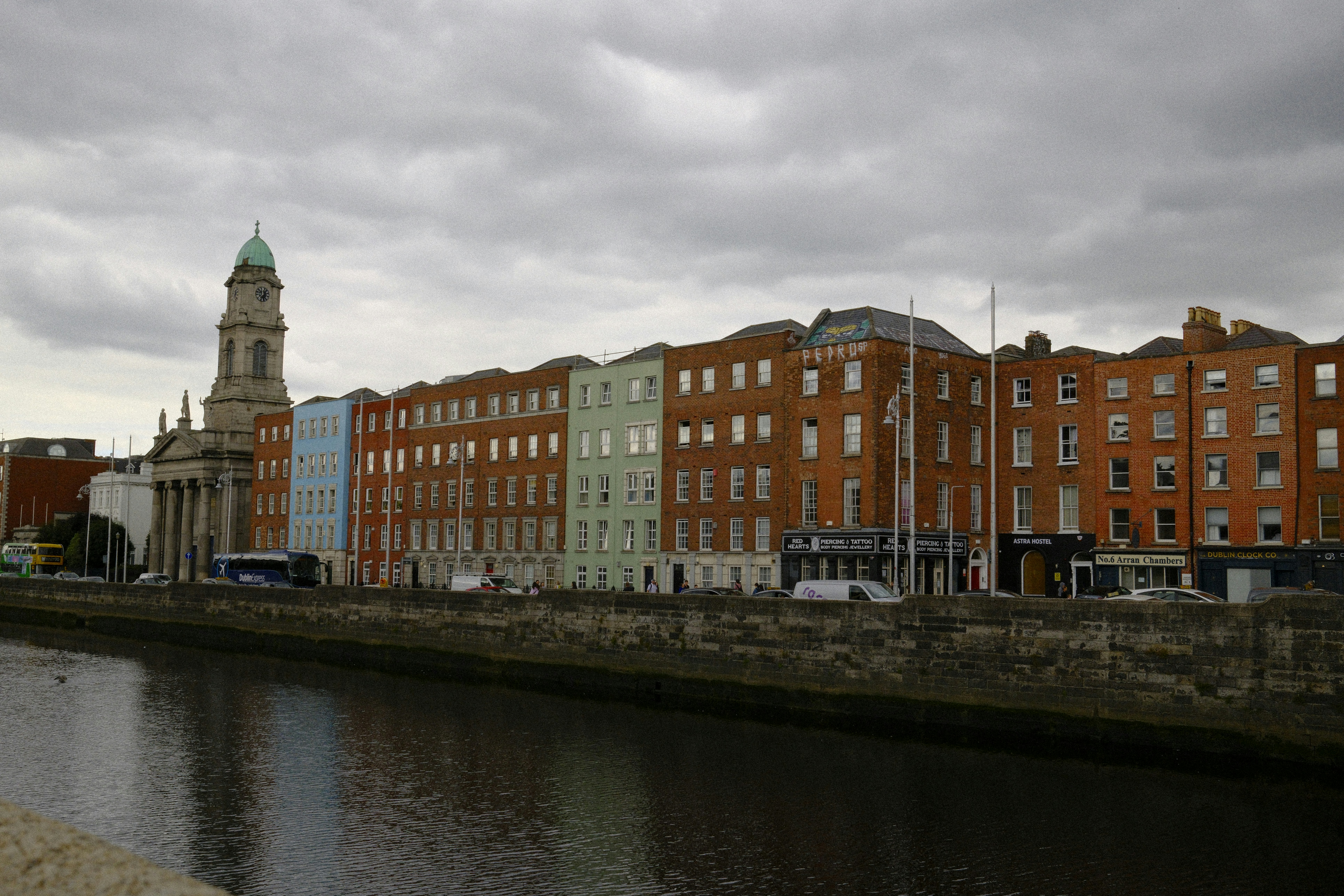 Buildings line a river under a cloudy sky.