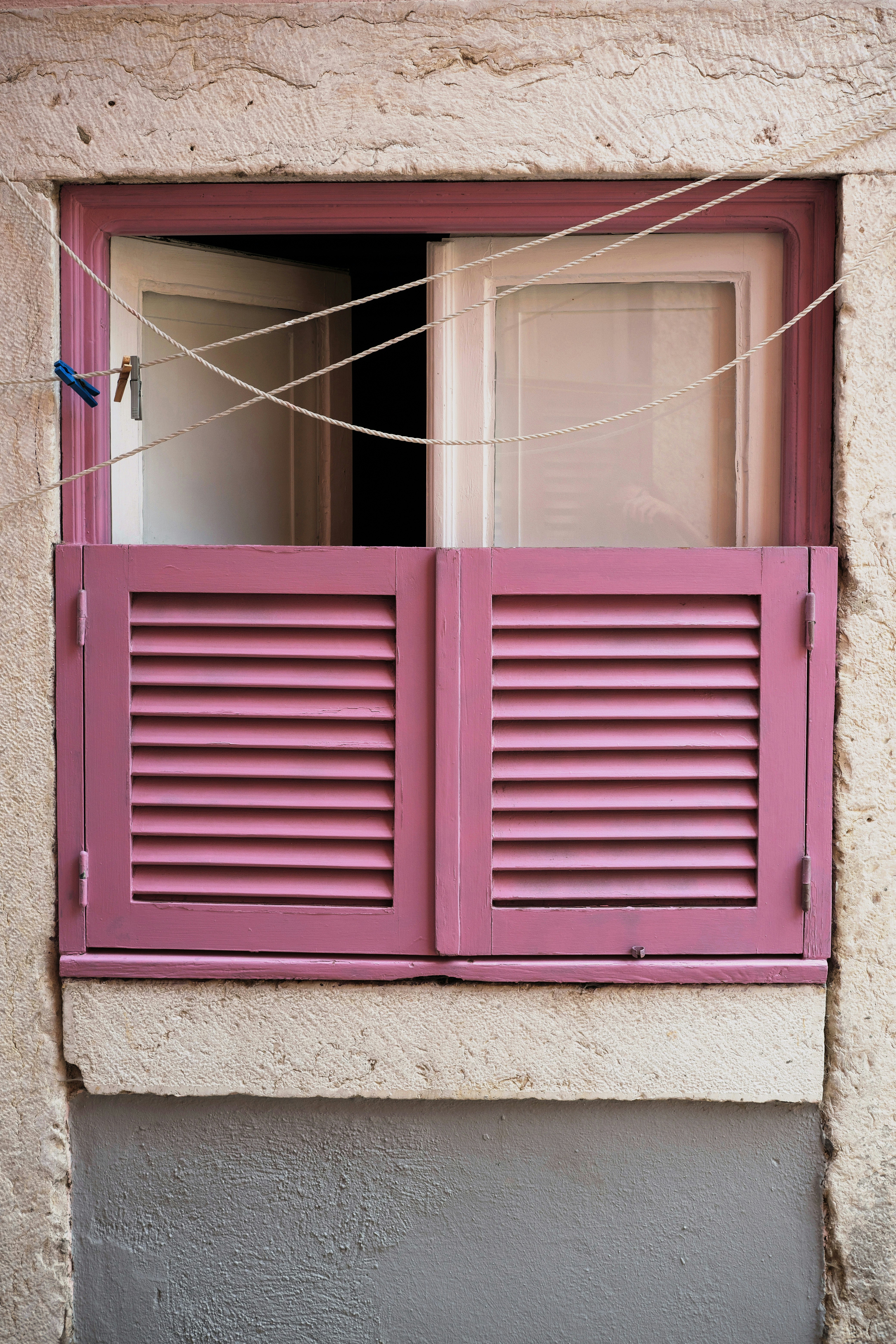 Las persianas rosas adornan una ventana abierta con un tendedero