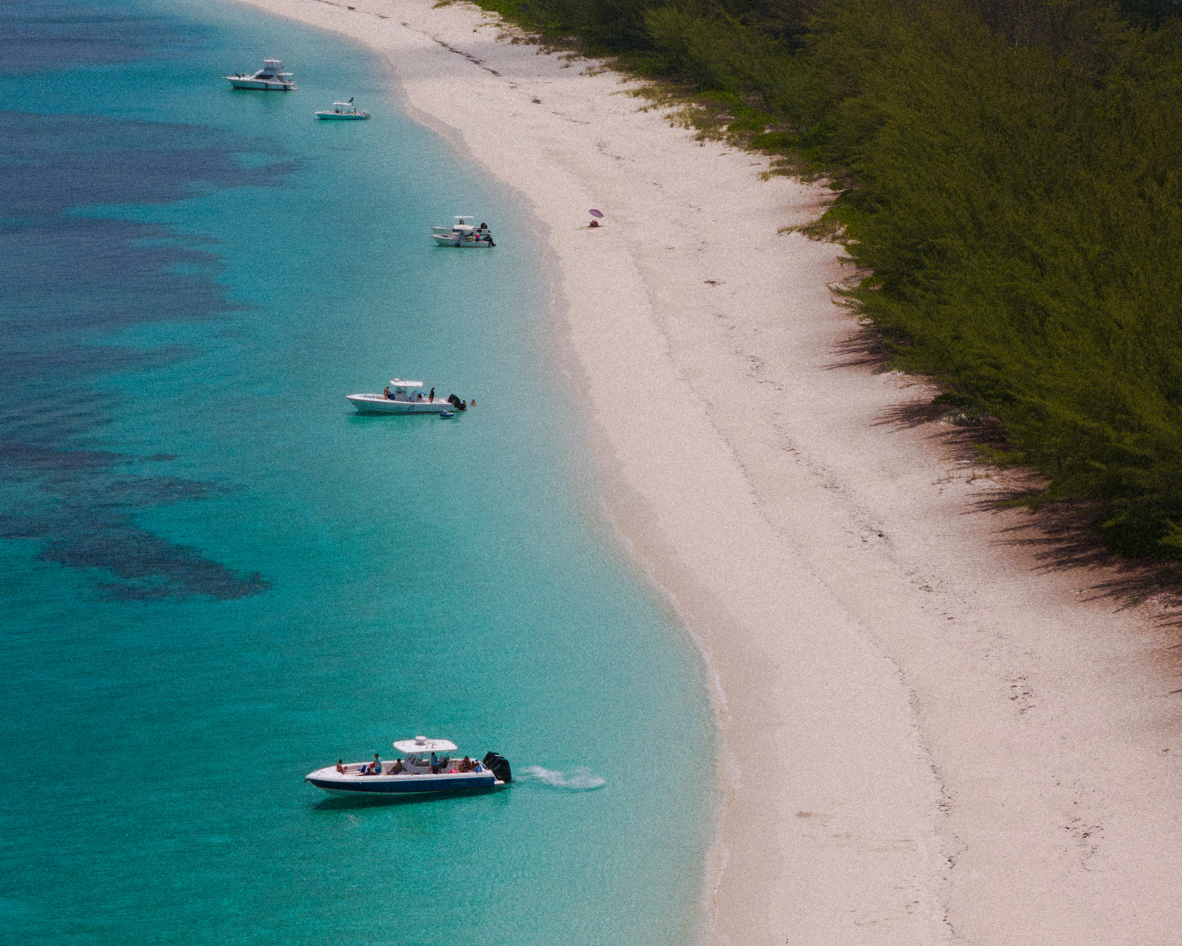 Boats anchored in turquoise water off a white-sand Bahamian beach