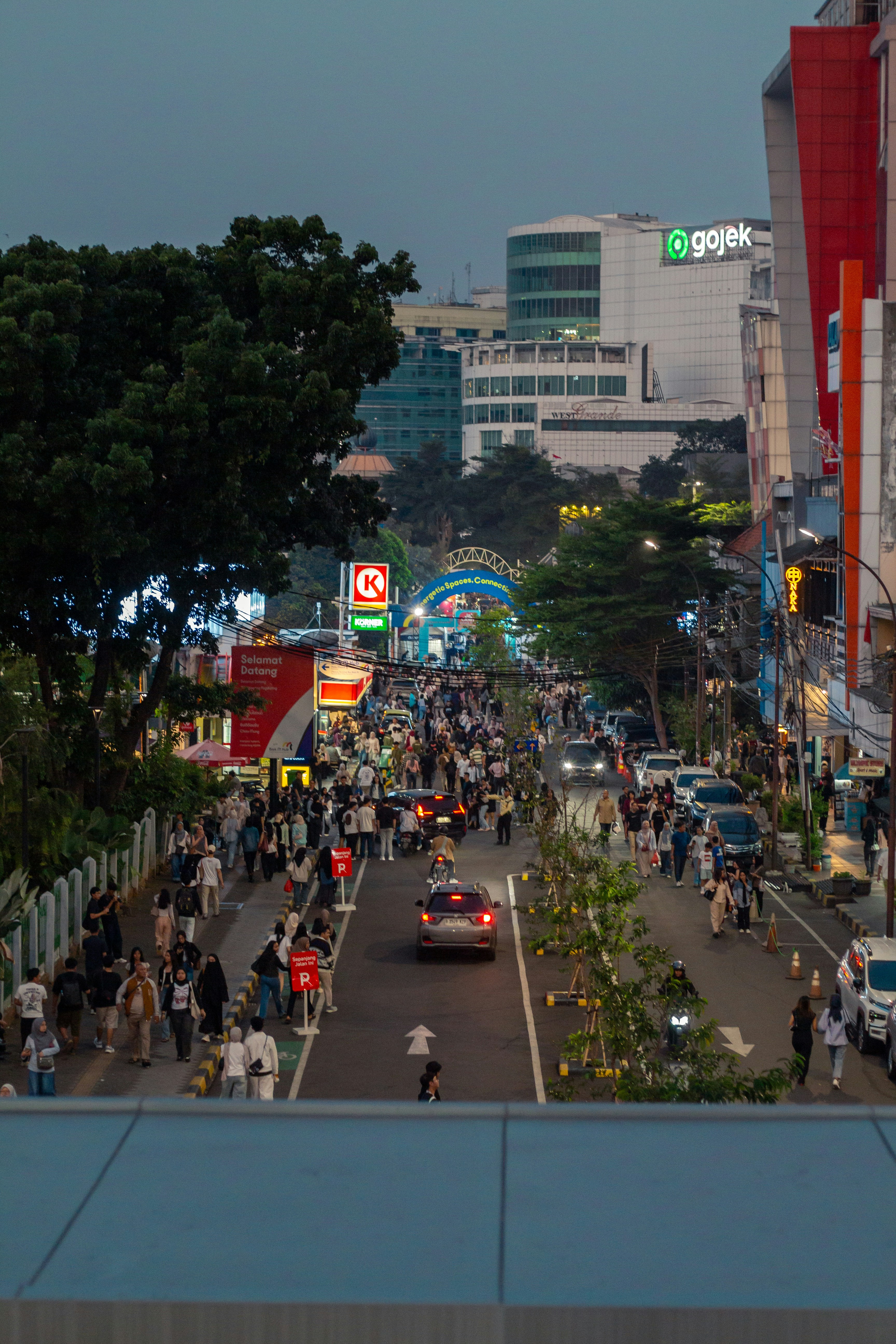 A busy street scene at dusk with many people.