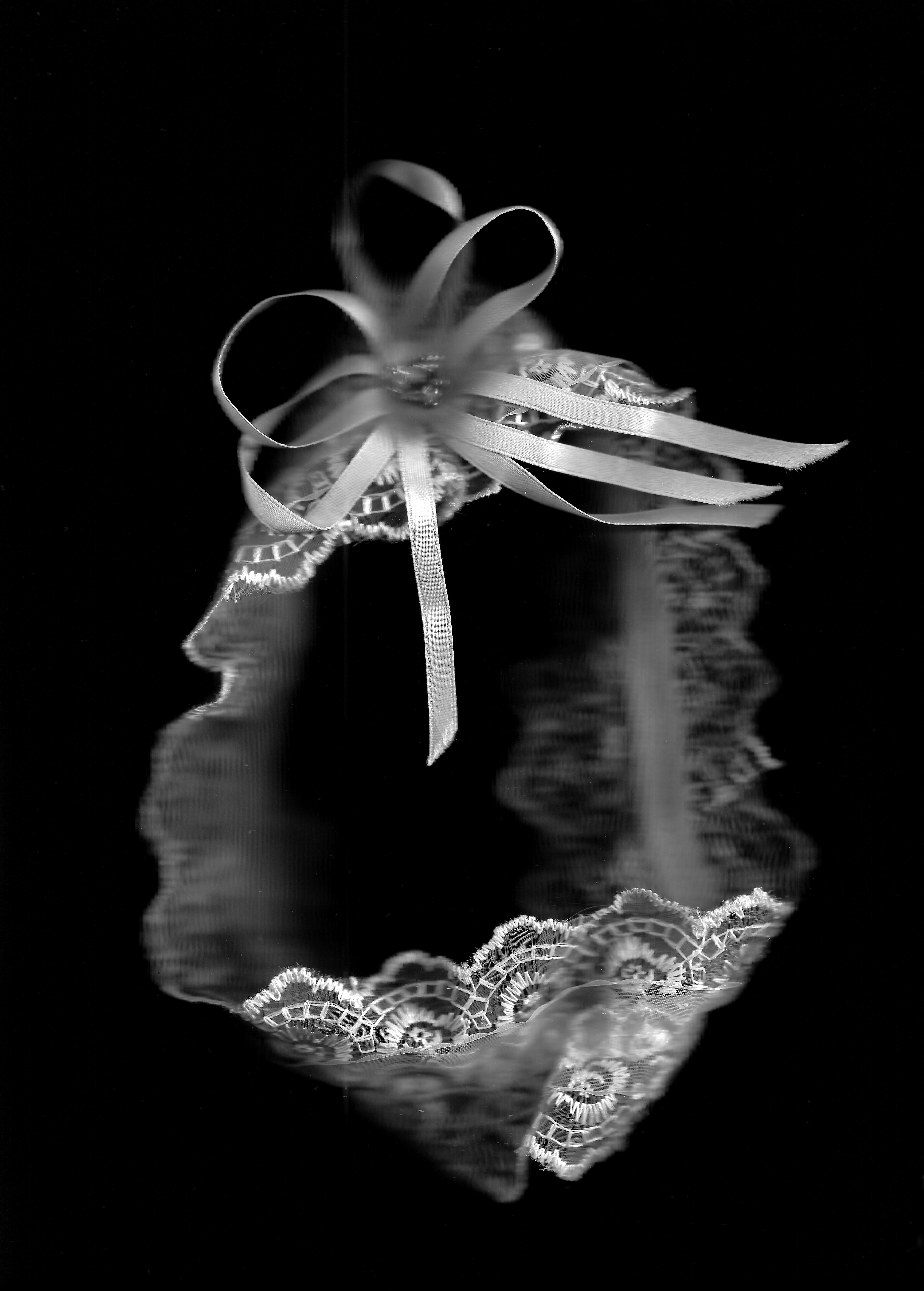 A lacy wedding garter hangs against a black background.