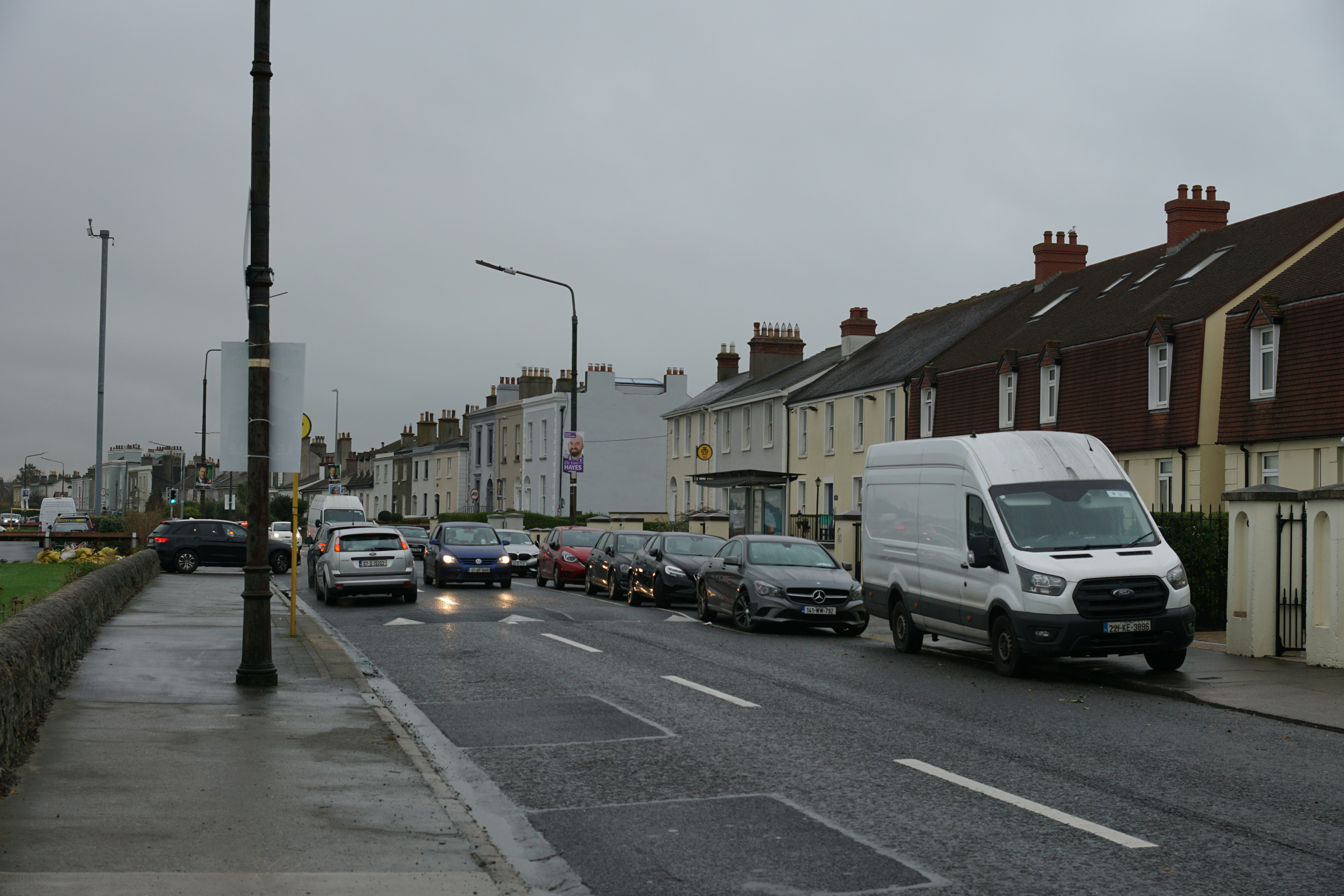 Cars are driving on a road next to houses.