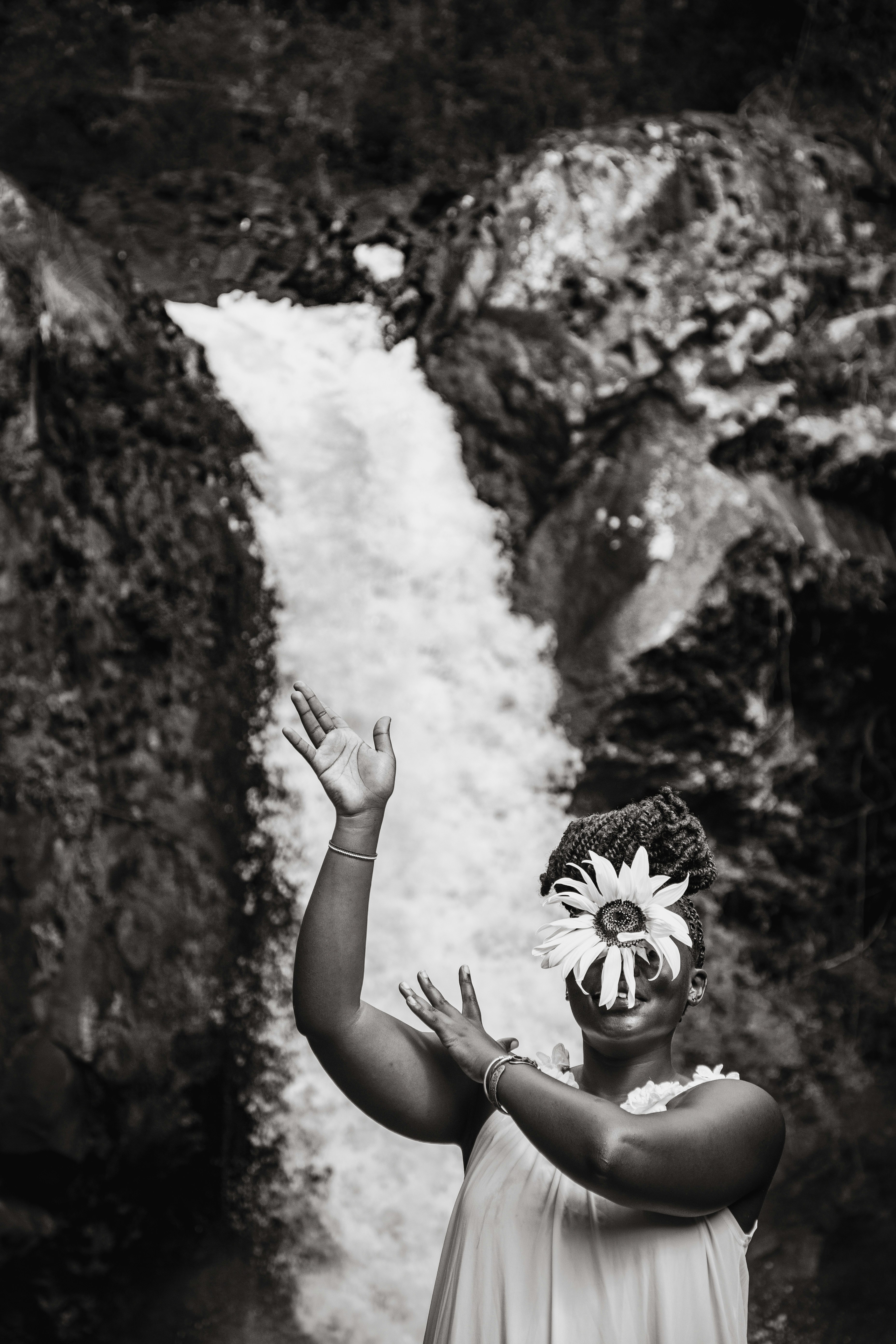 Woman poses with a flower in front of a waterfall.