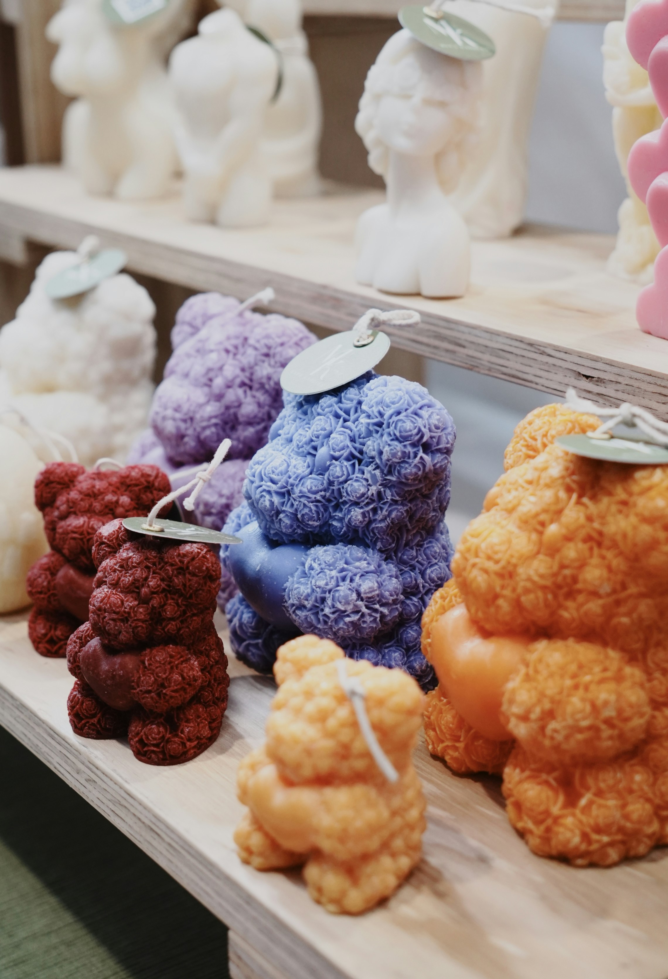 Decorative shaped candles rest on light wooden store shelves.