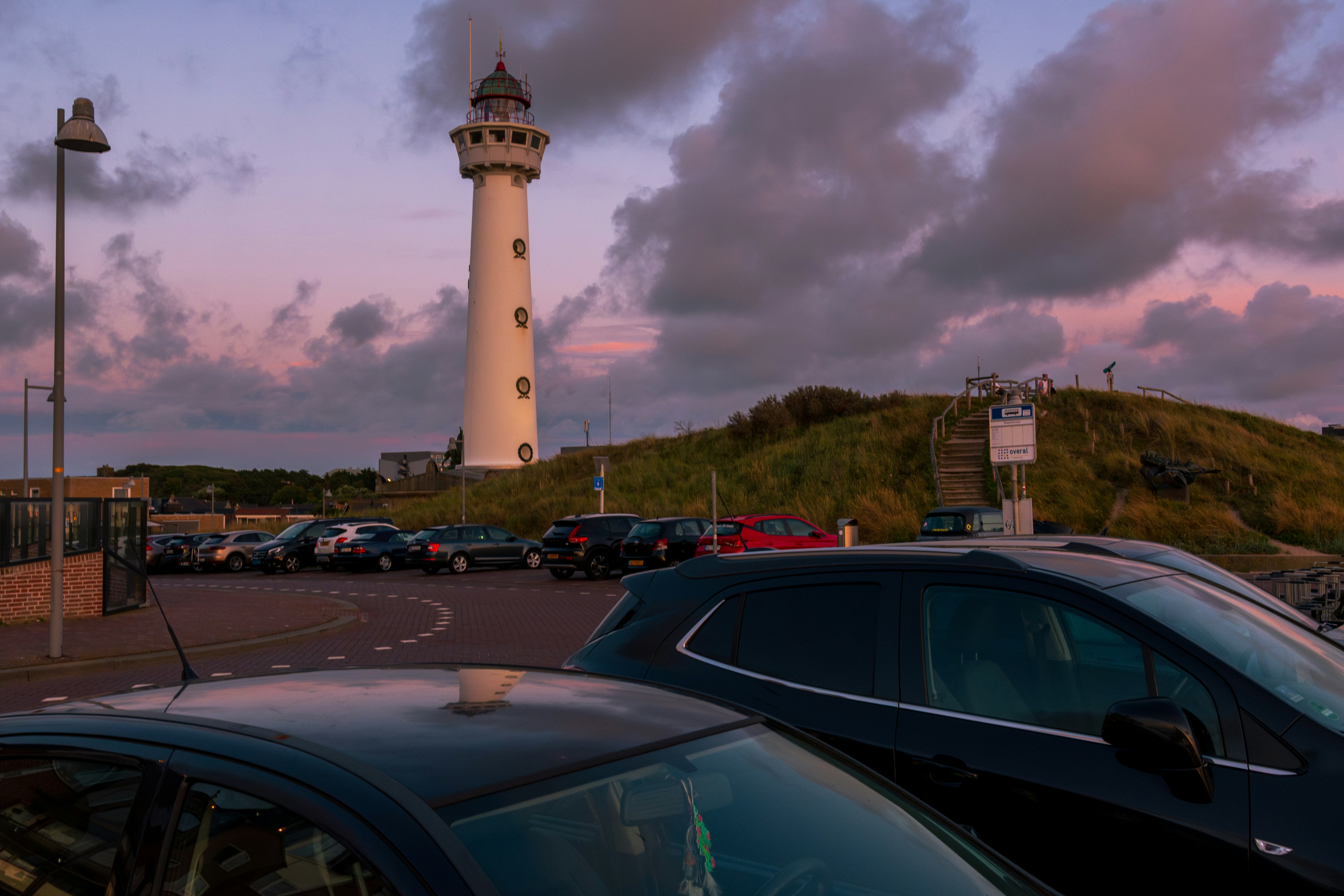 Faro e auto sotto un bellissimo cielo serale.