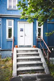 A blue house with white doors and concrete steps.