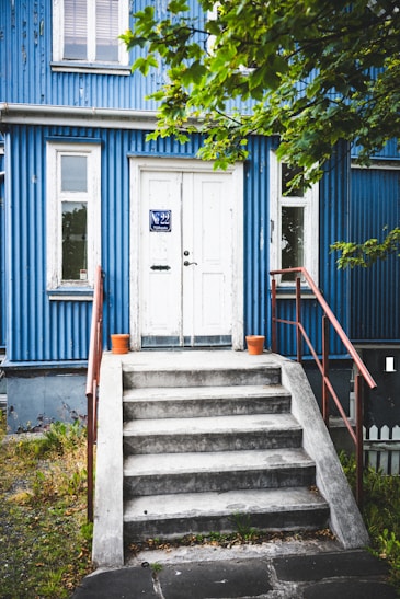A blue house with white doors and concrete steps.