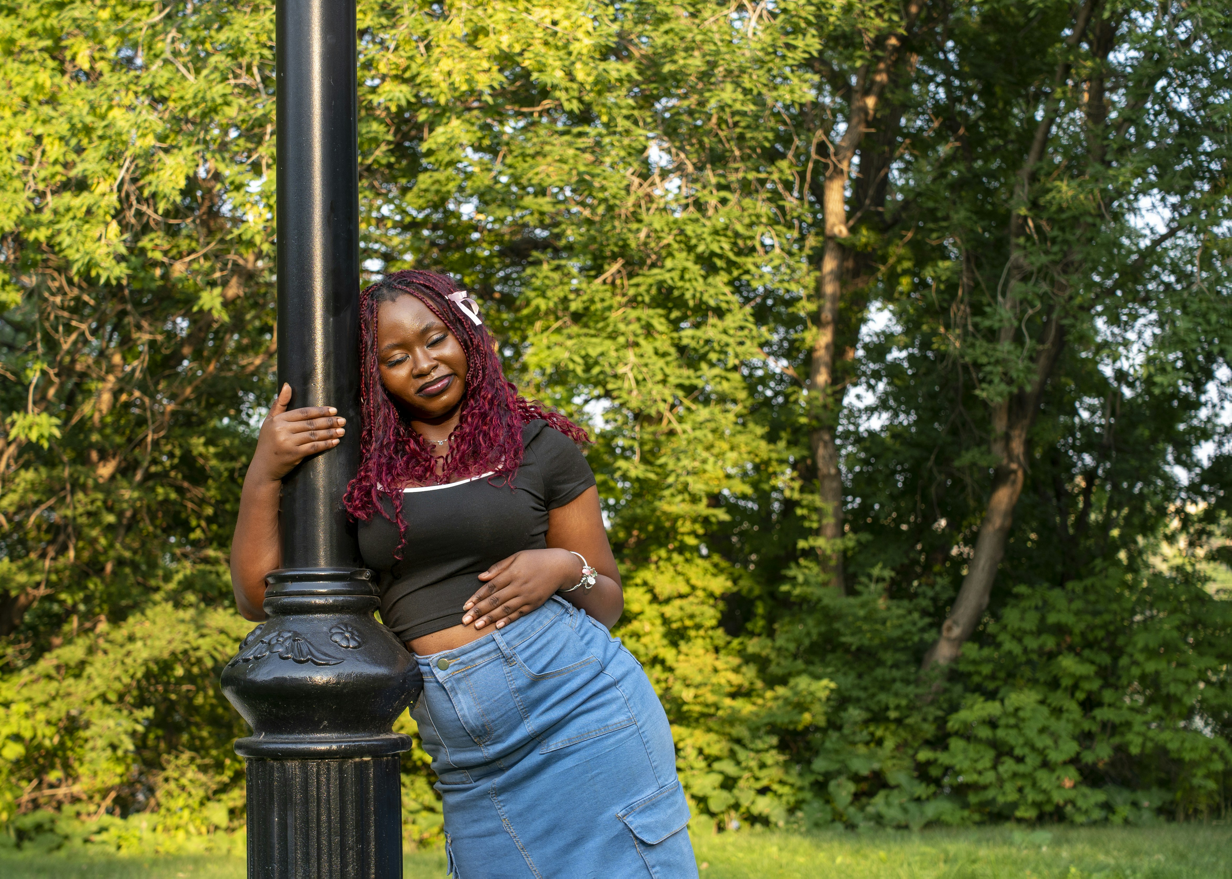 Woman leans against a lamp post in a park.