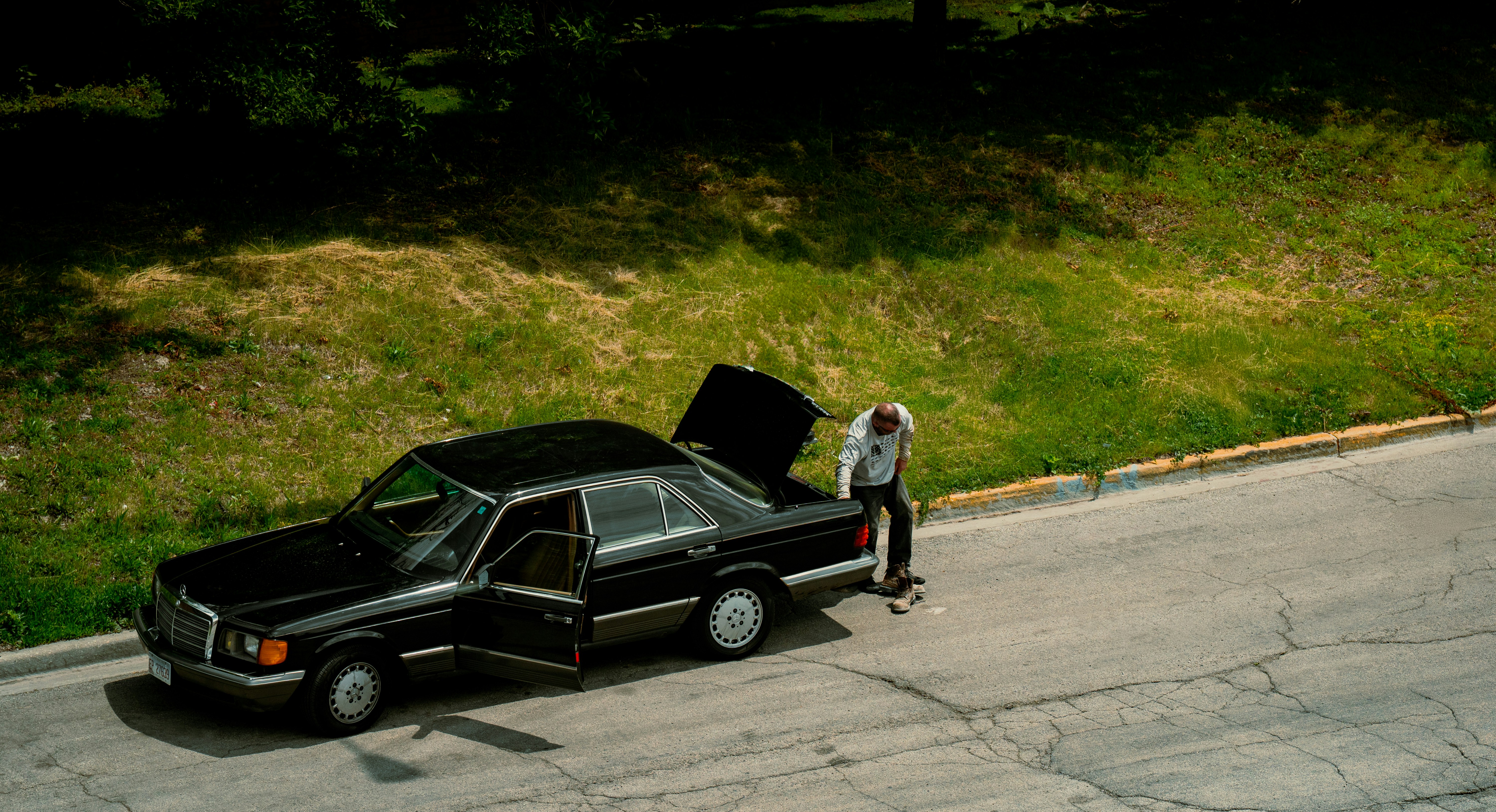 Man is placing something in a black car's trunk.