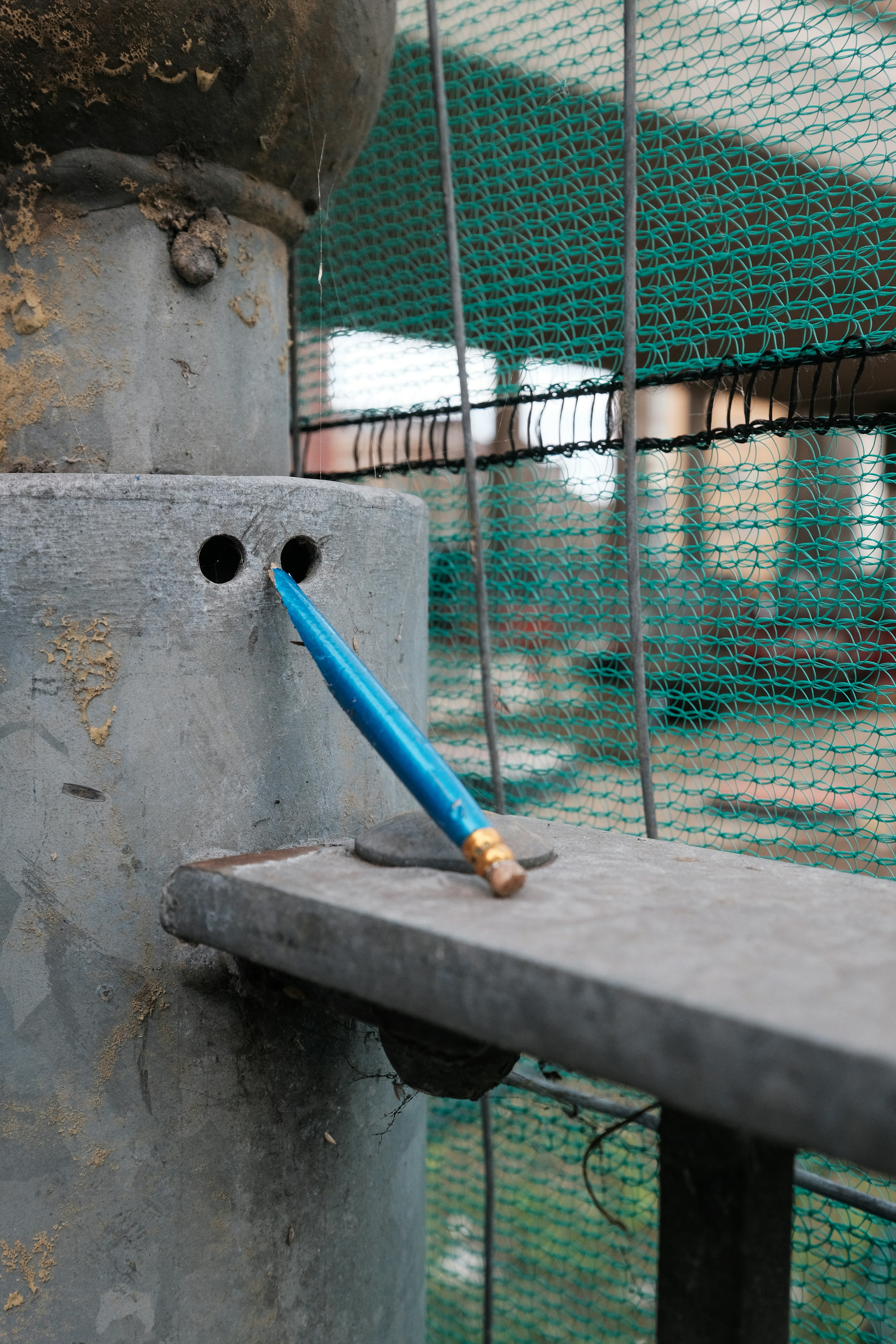 A blue pencil rests on a grey structure.