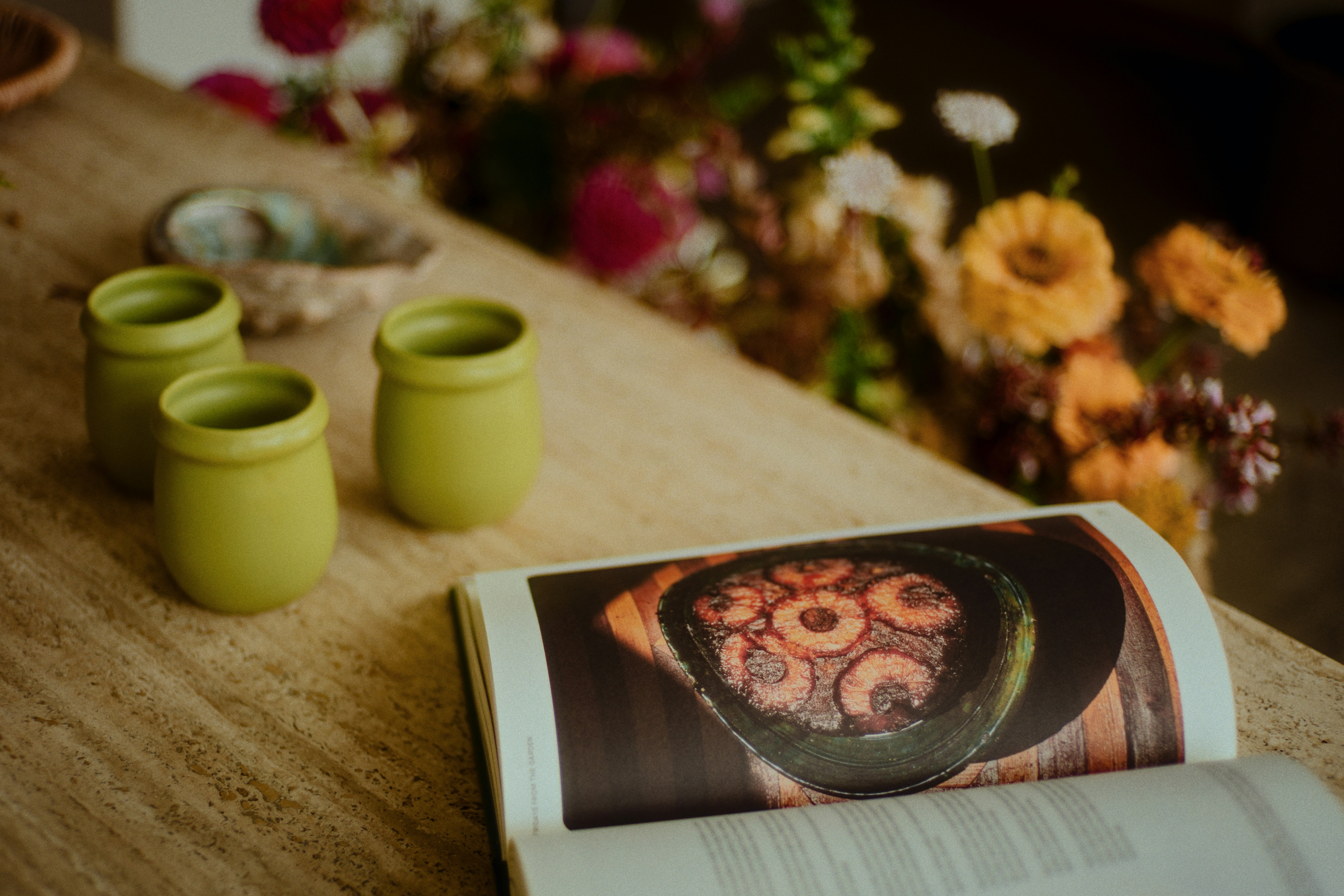 An open book, jars, and flowers on a table.