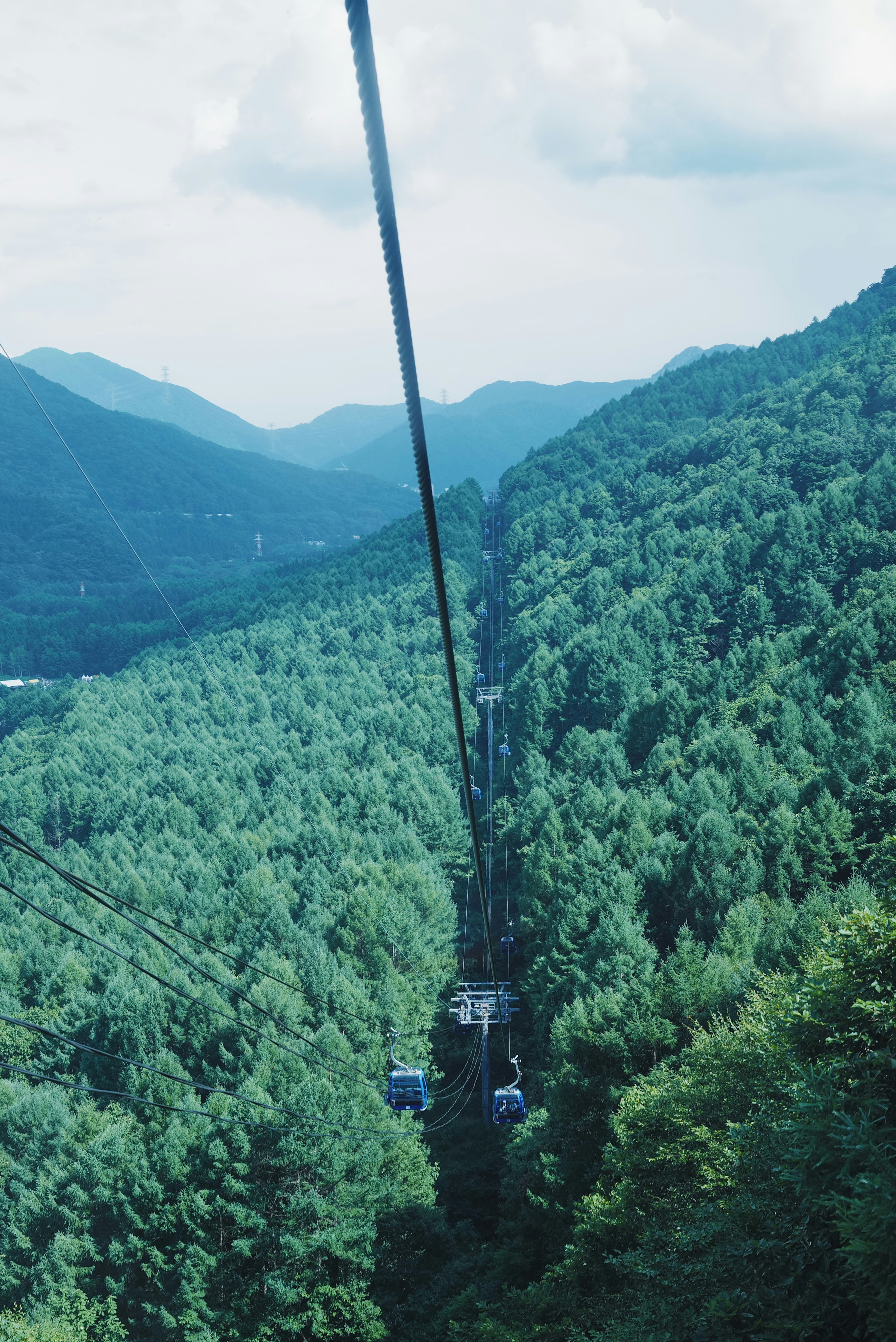 Cable cars ascend through a green mountain valley.
