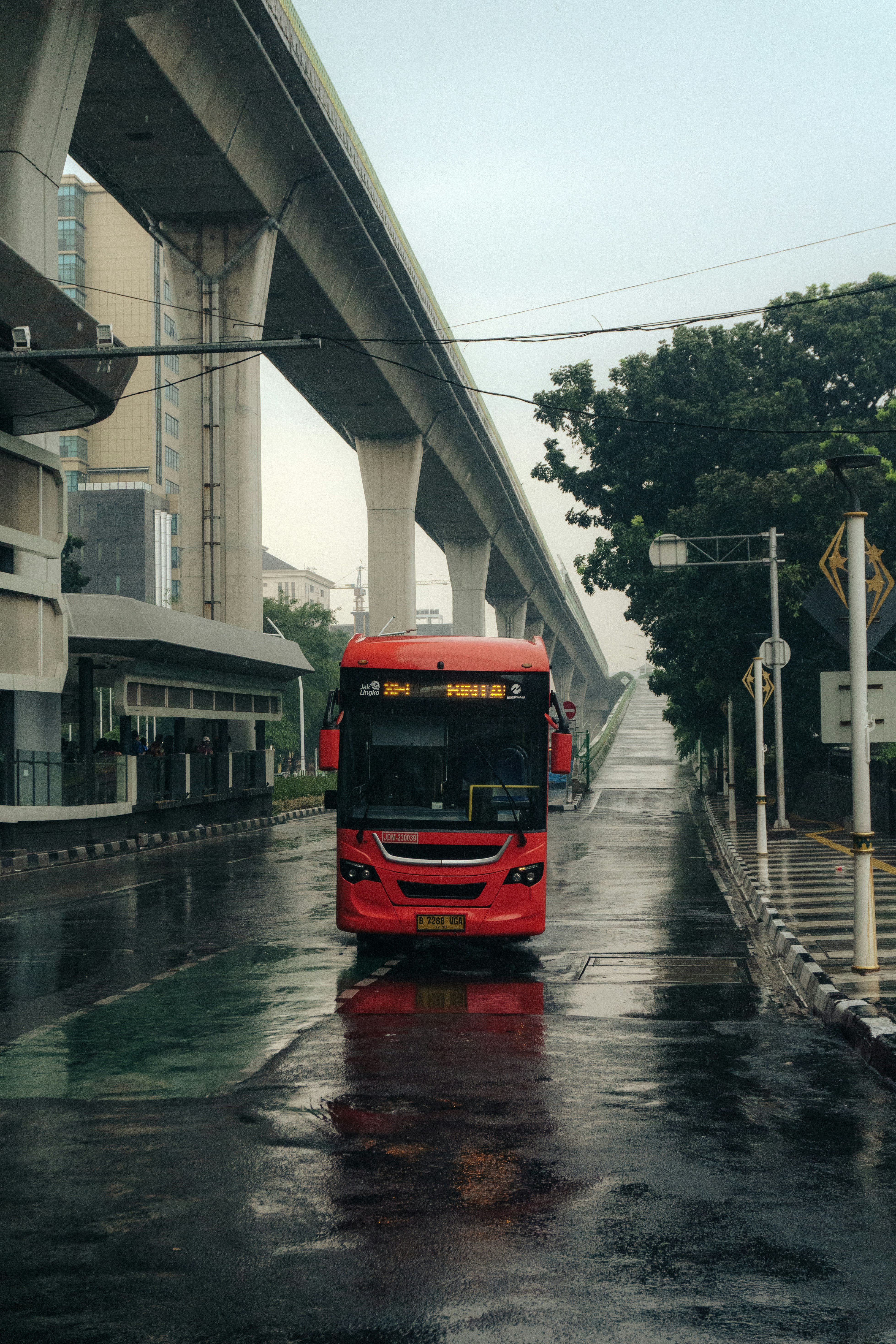 A red bus travels down a wet city street.