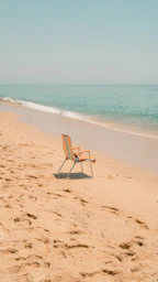 A beach chair sits alone on the sandy shore.