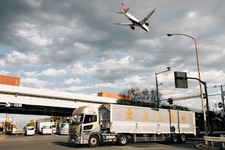 An airplane flies above a truck on a road.