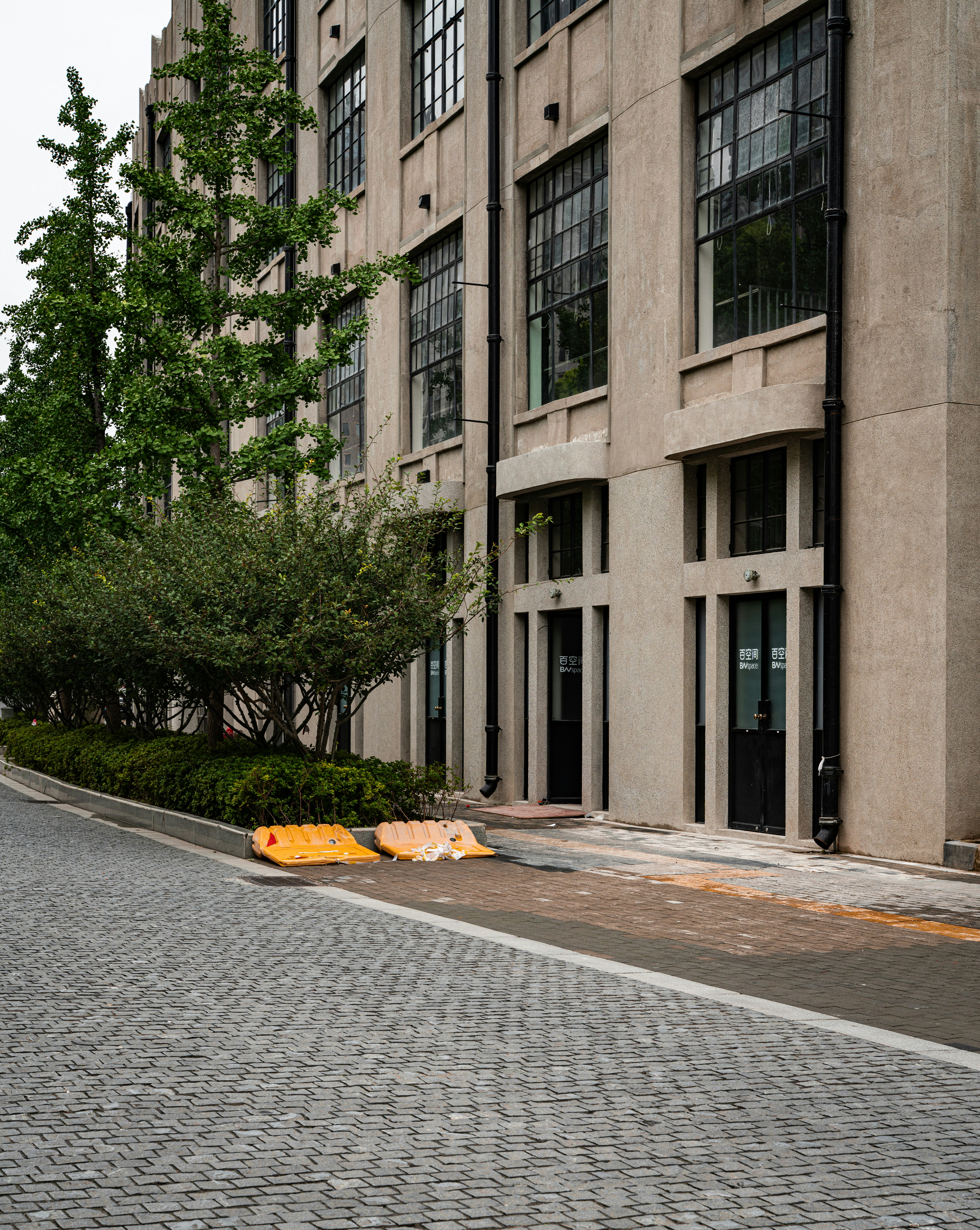 An industrial building with green trees and an empty street.
