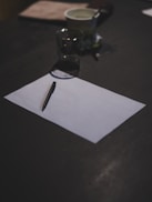 Blank paper and pen sit on a dark table.