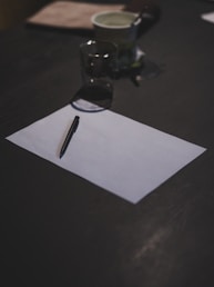 Blank paper and pen sit on a dark table.