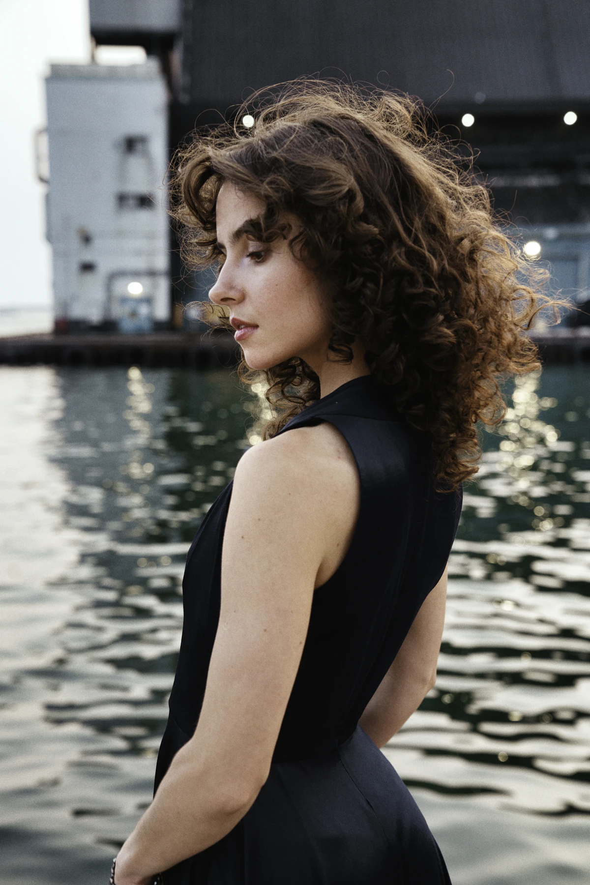 A woman with curly hair posing by the water