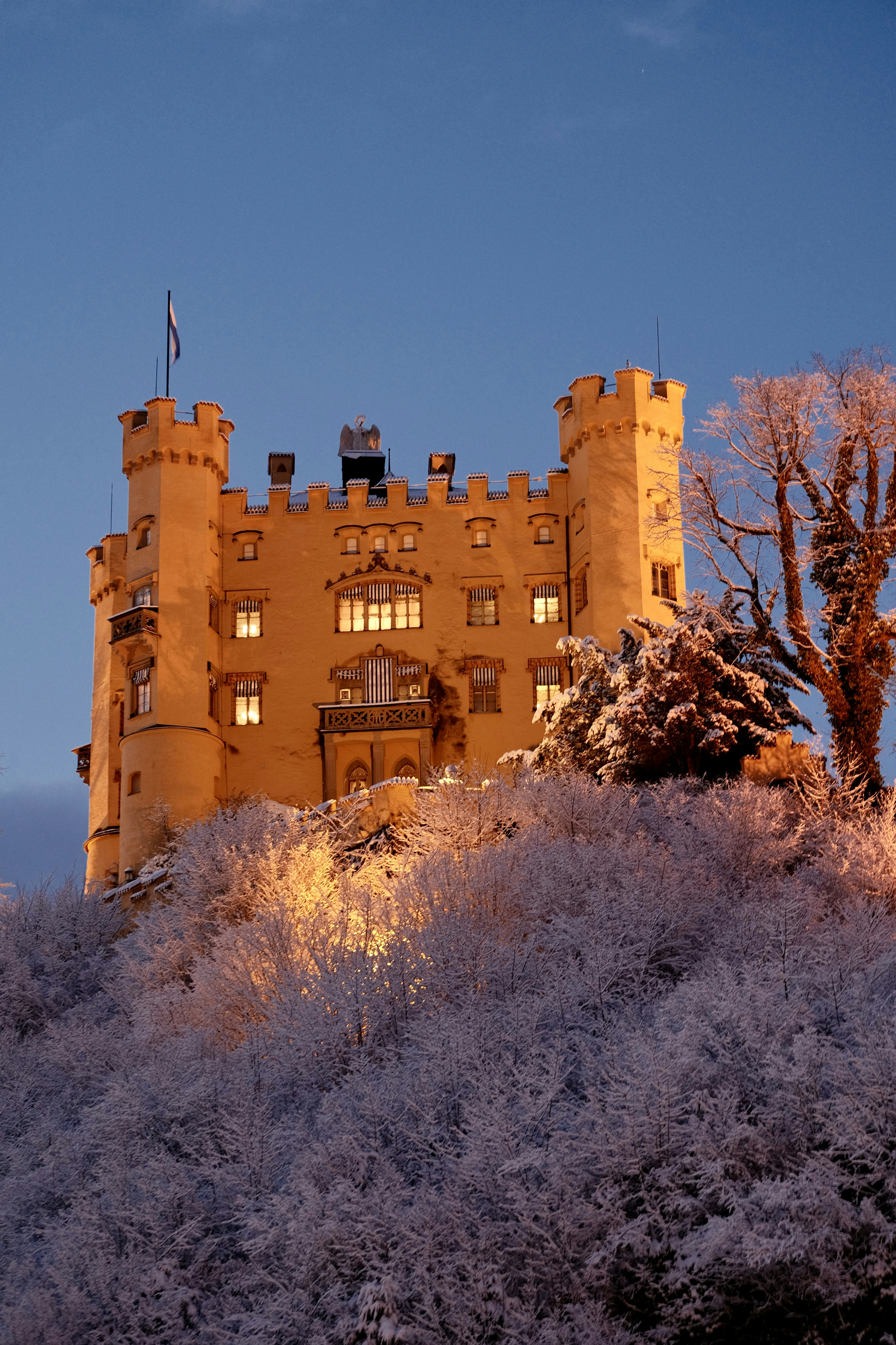 A castle illuminated at dusk atop a snowy hill.