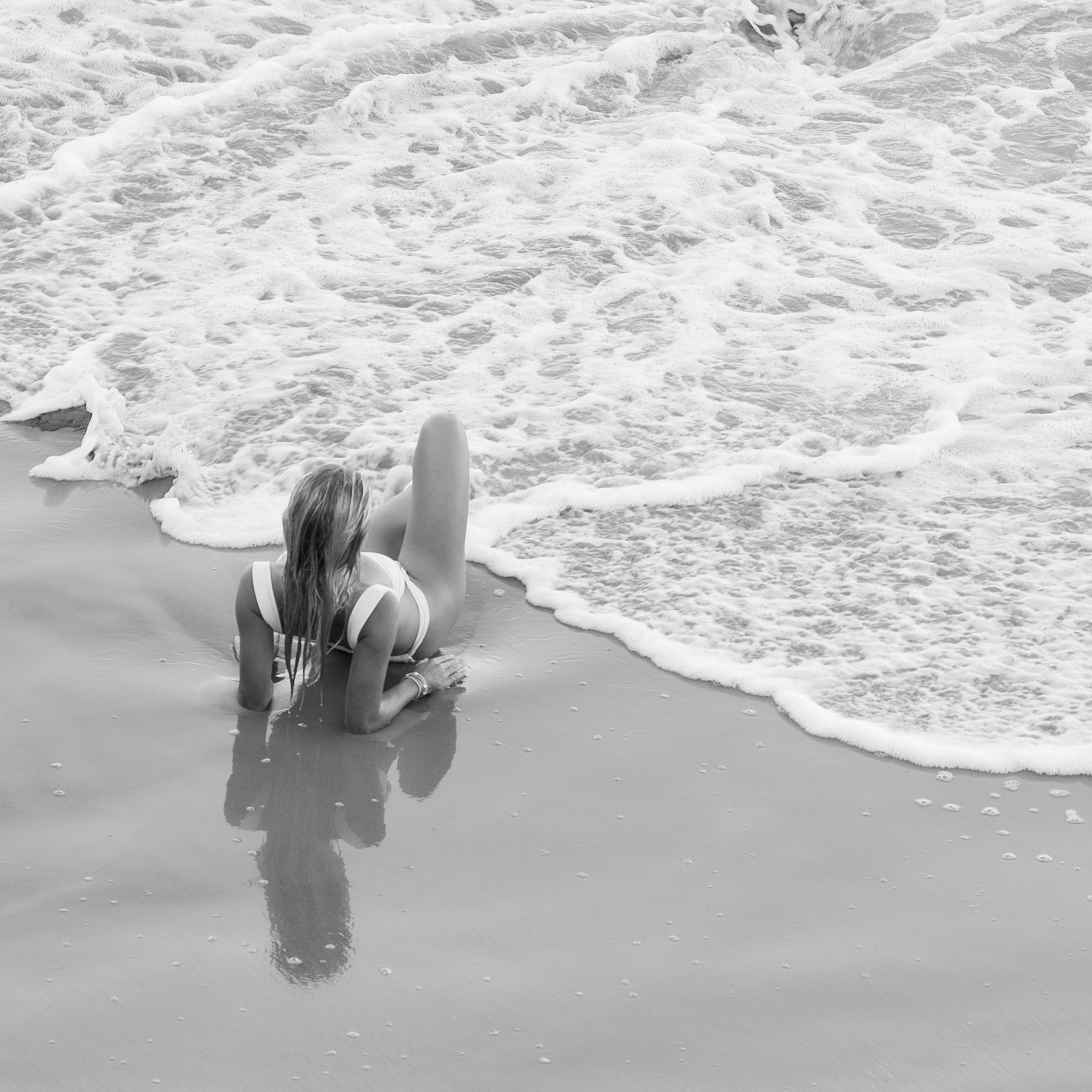 Woman lays on the beach as waves approach.