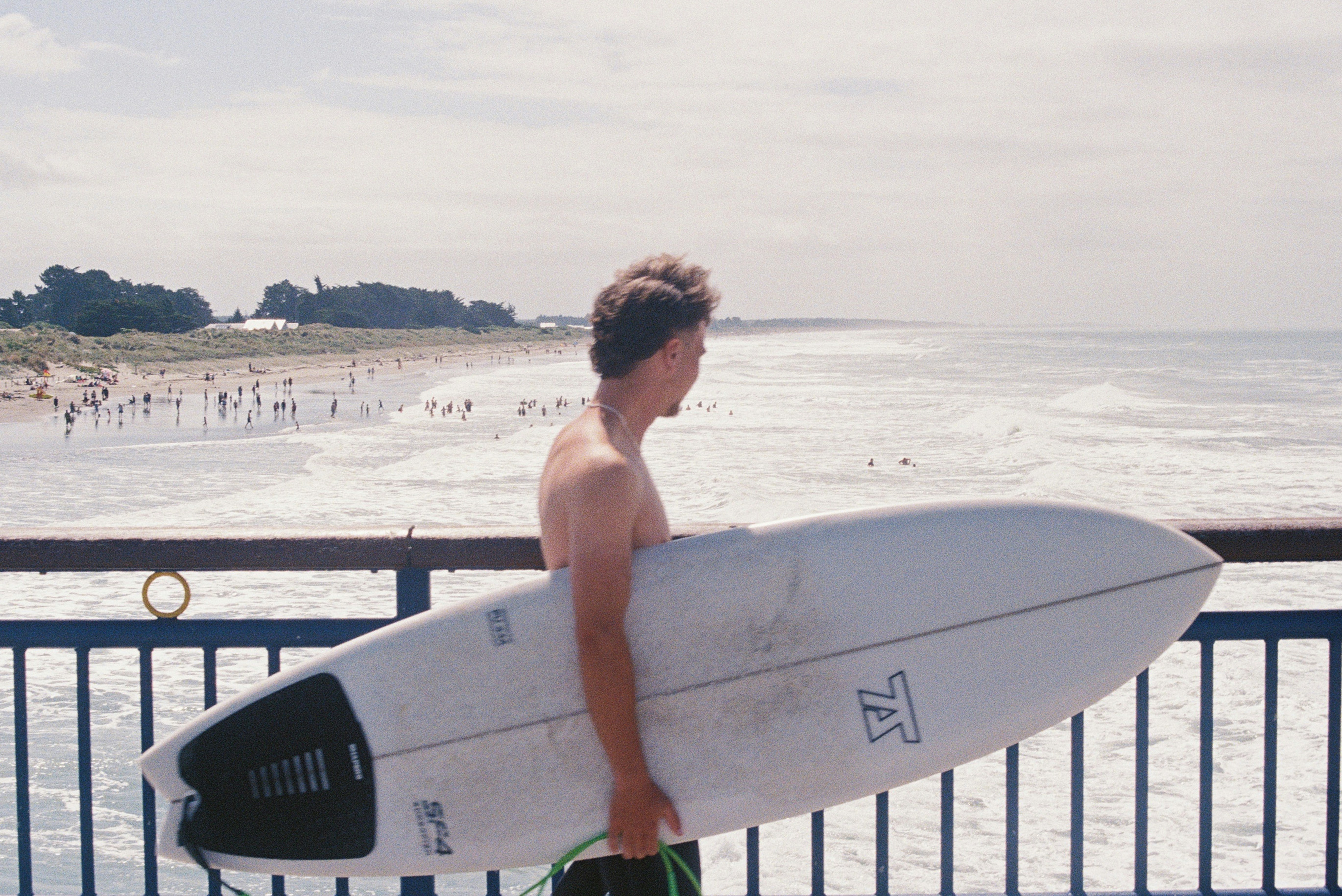 A surfer walks along a pier with his board.