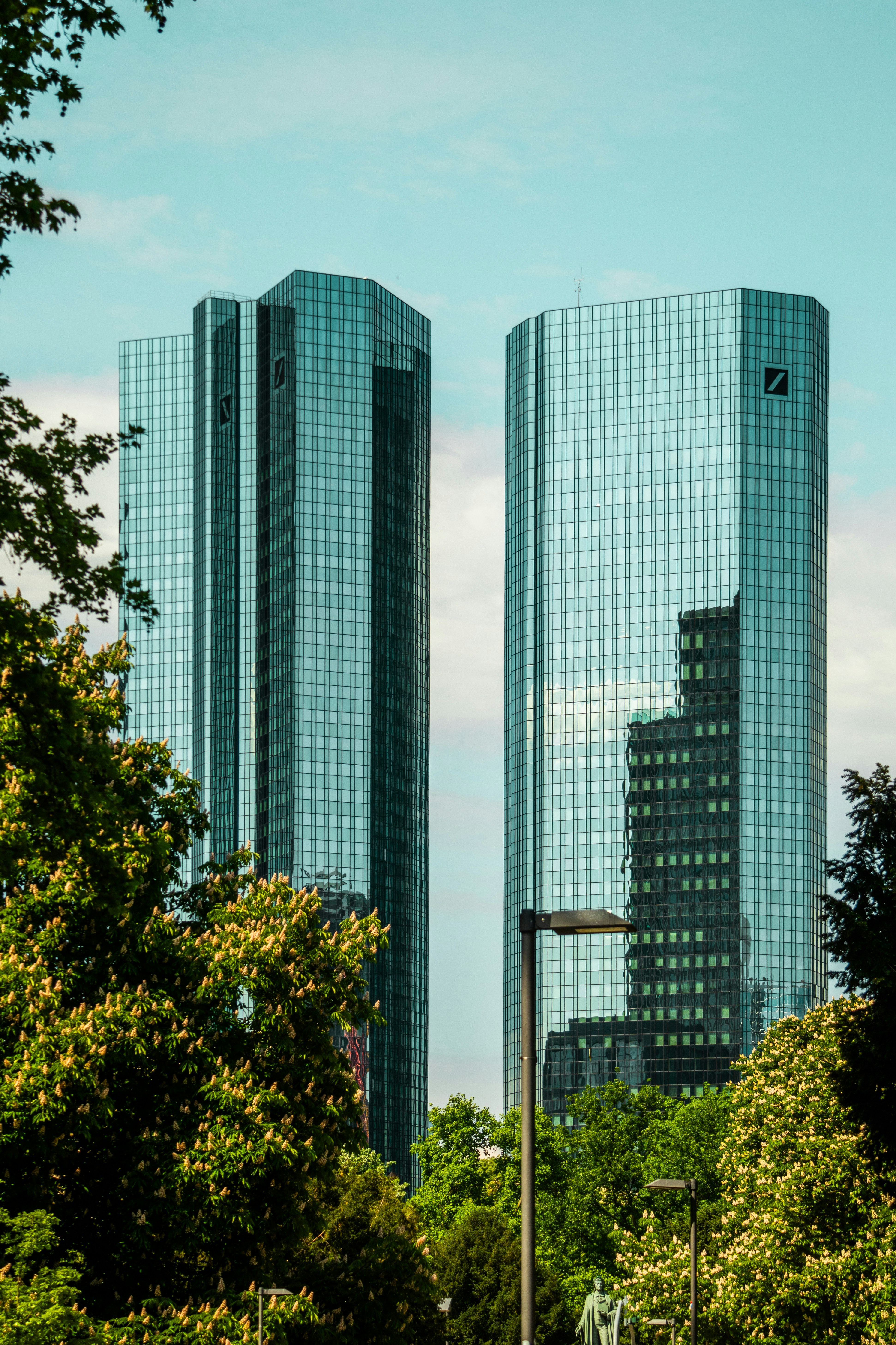 Two tall modern skyscrapers are framed by trees.