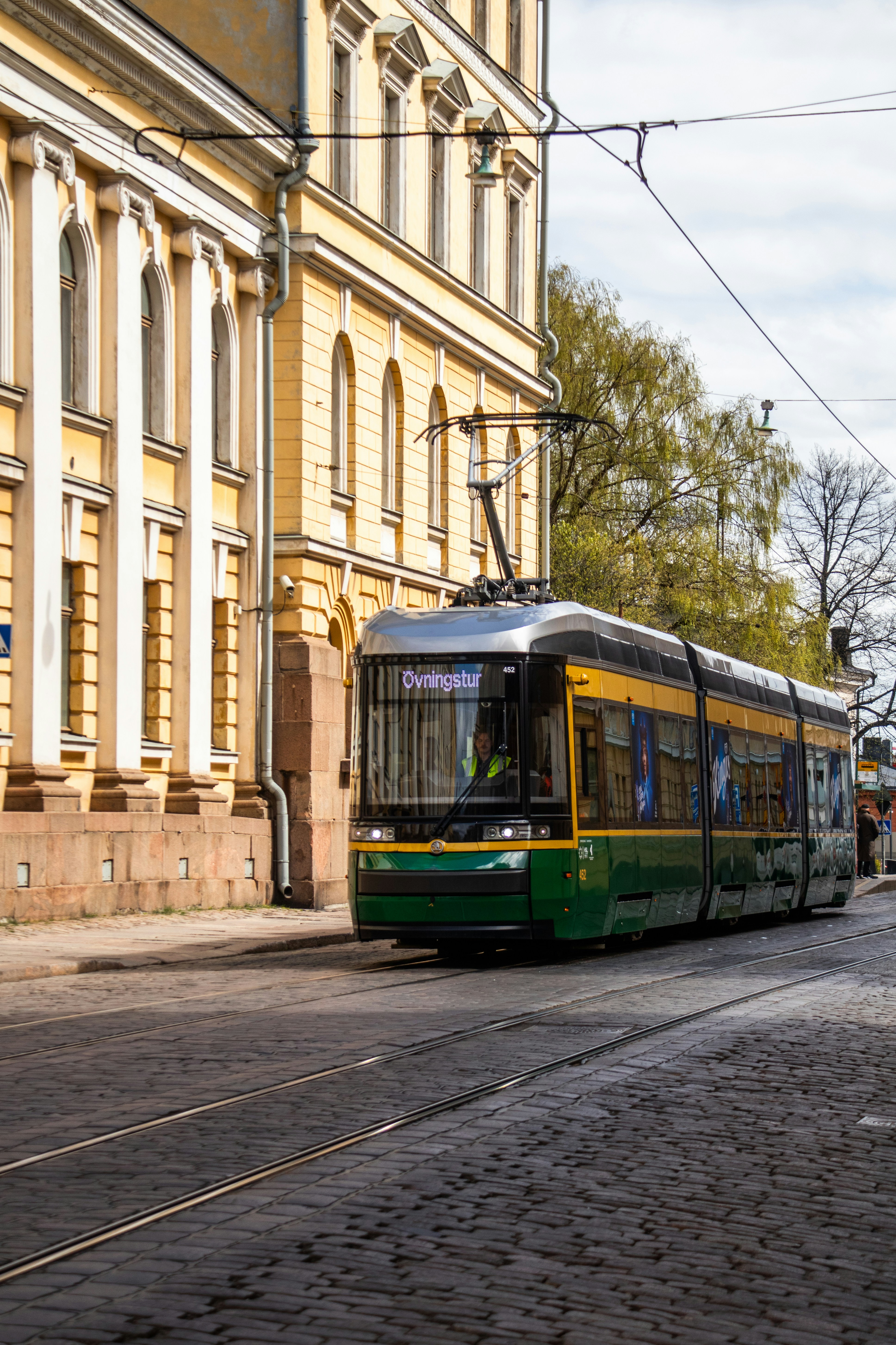 A green tram travels past a classic yellow building.