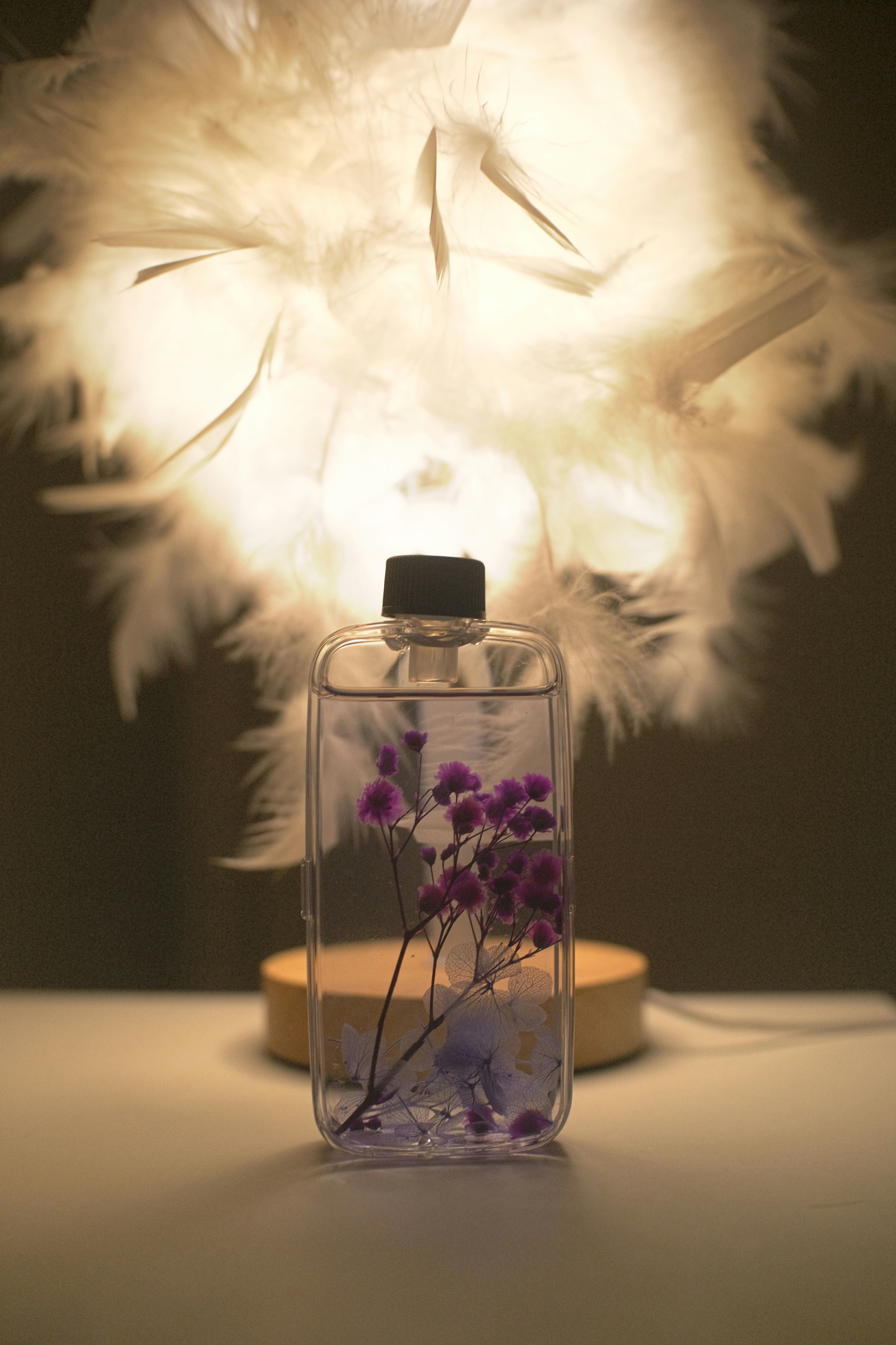A bottle with purple flowers and a feathered lamp.